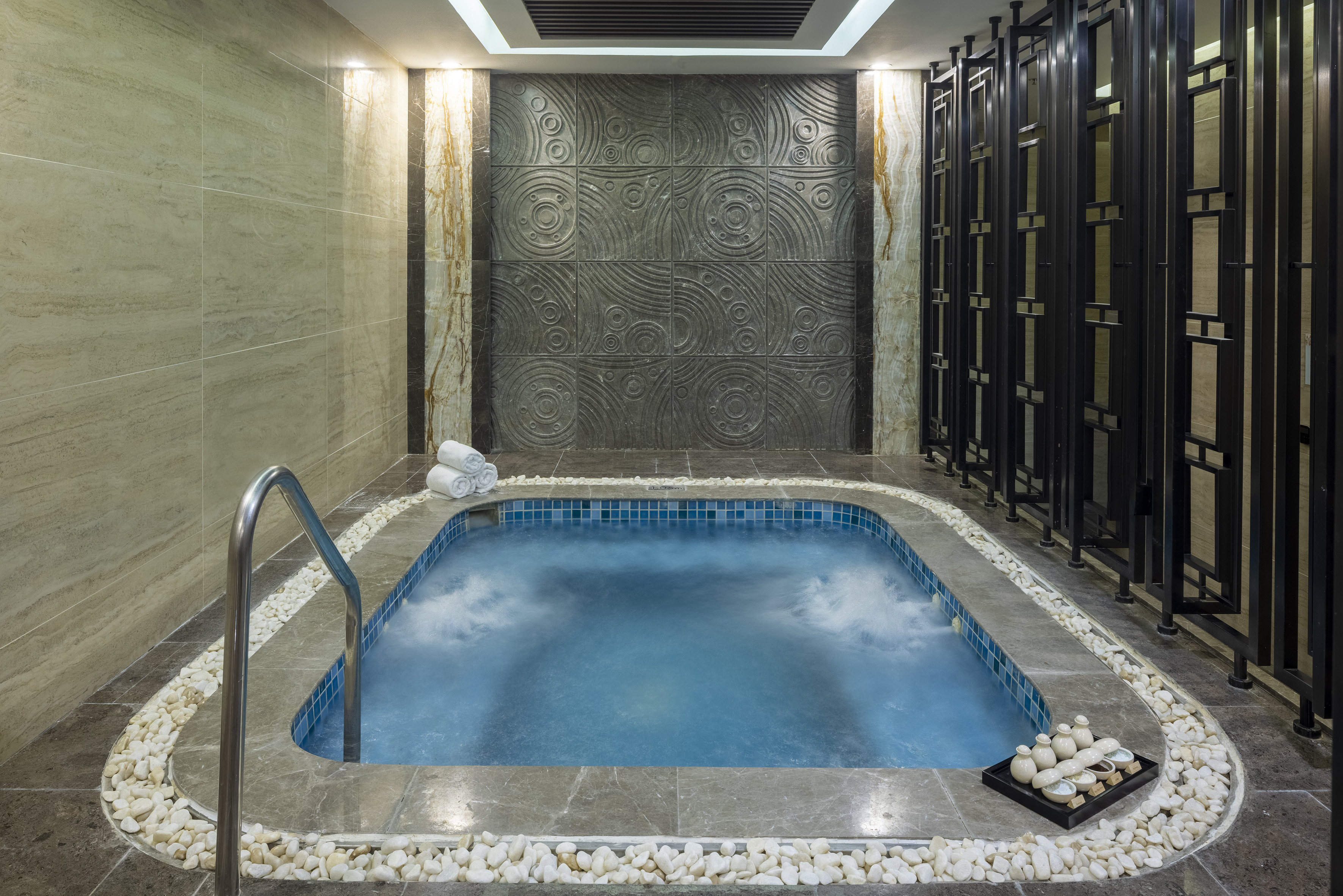 Indoor spa jacuzzi with textured stone walls, bubbling water, and clean towels.