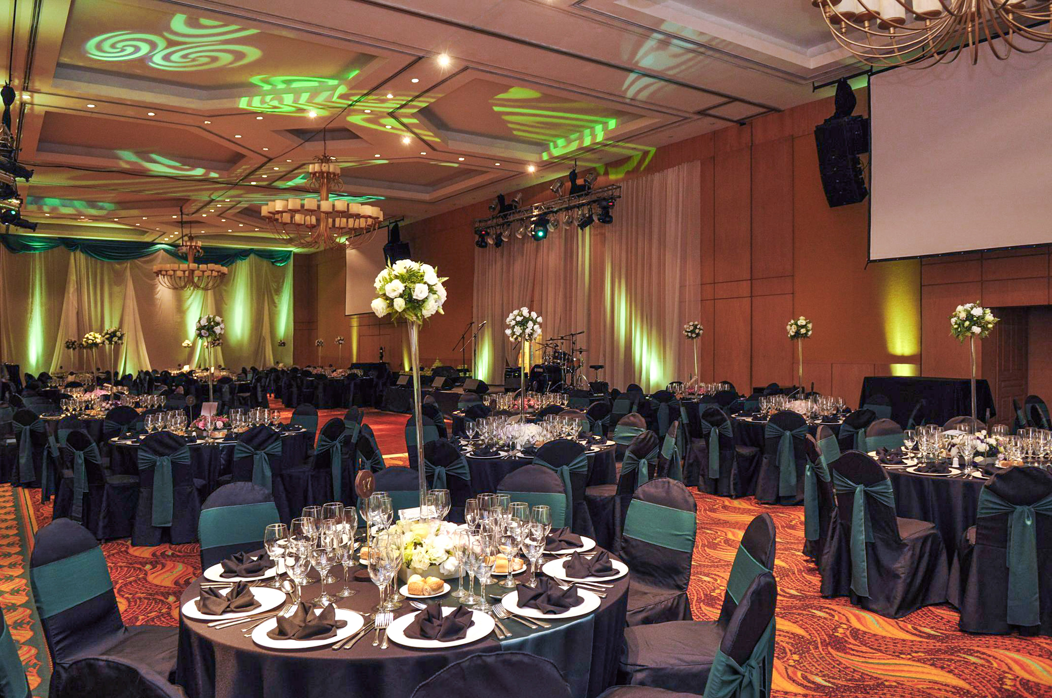 Set ballroom for formal event, black & green decor, stage, floral centerpieces.