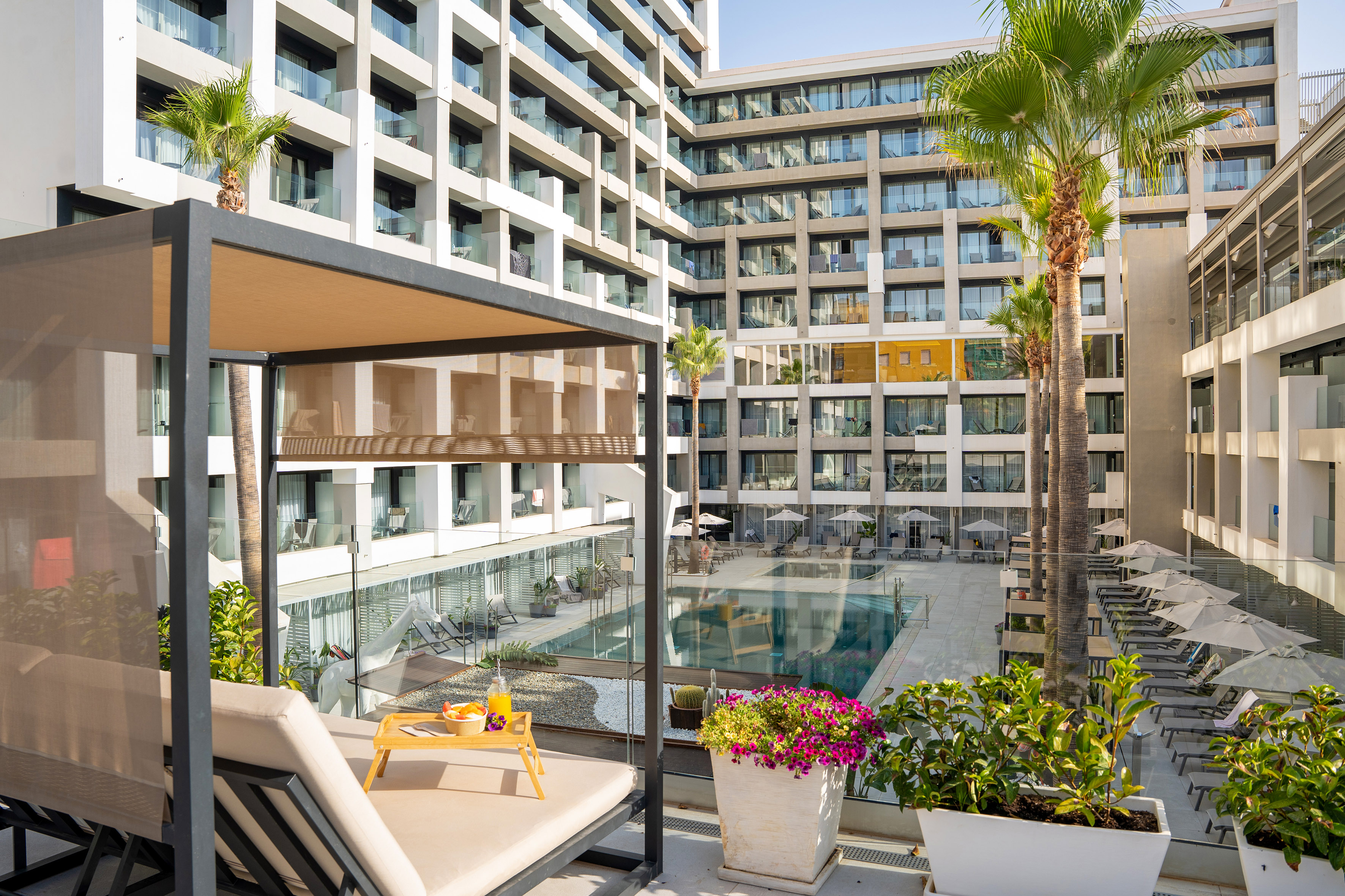 Sunny resort pool, modern hotel, palm trees, and private cabana.