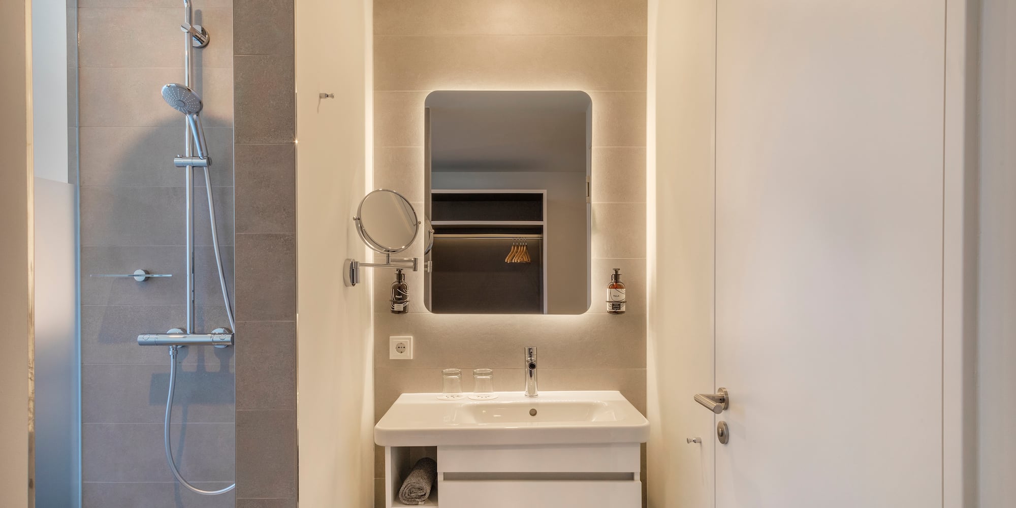 Contemporary bathroom featuring shower, white sink vanity, and backlit mirror.