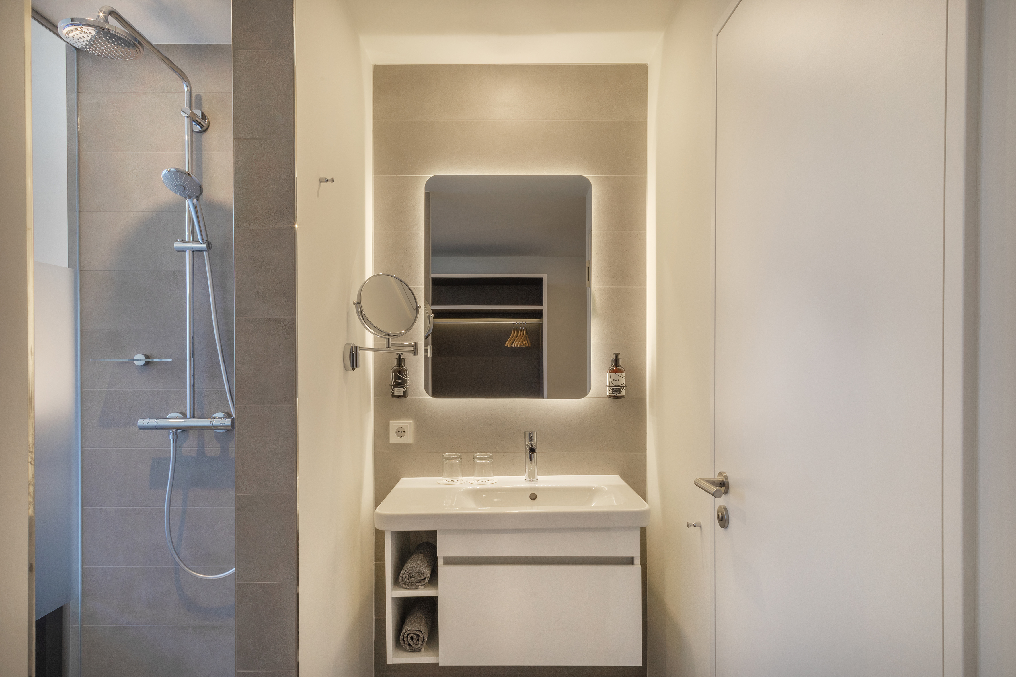 Contemporary bathroom featuring shower, white sink vanity, and backlit mirror.