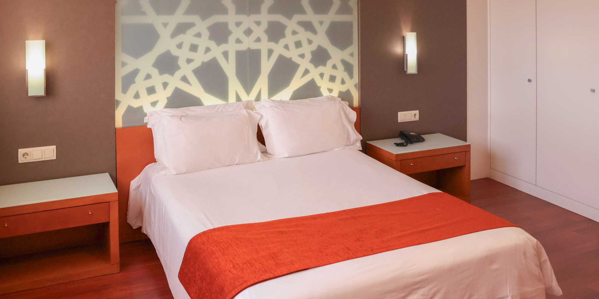 a bed with white sheets and orange blanket