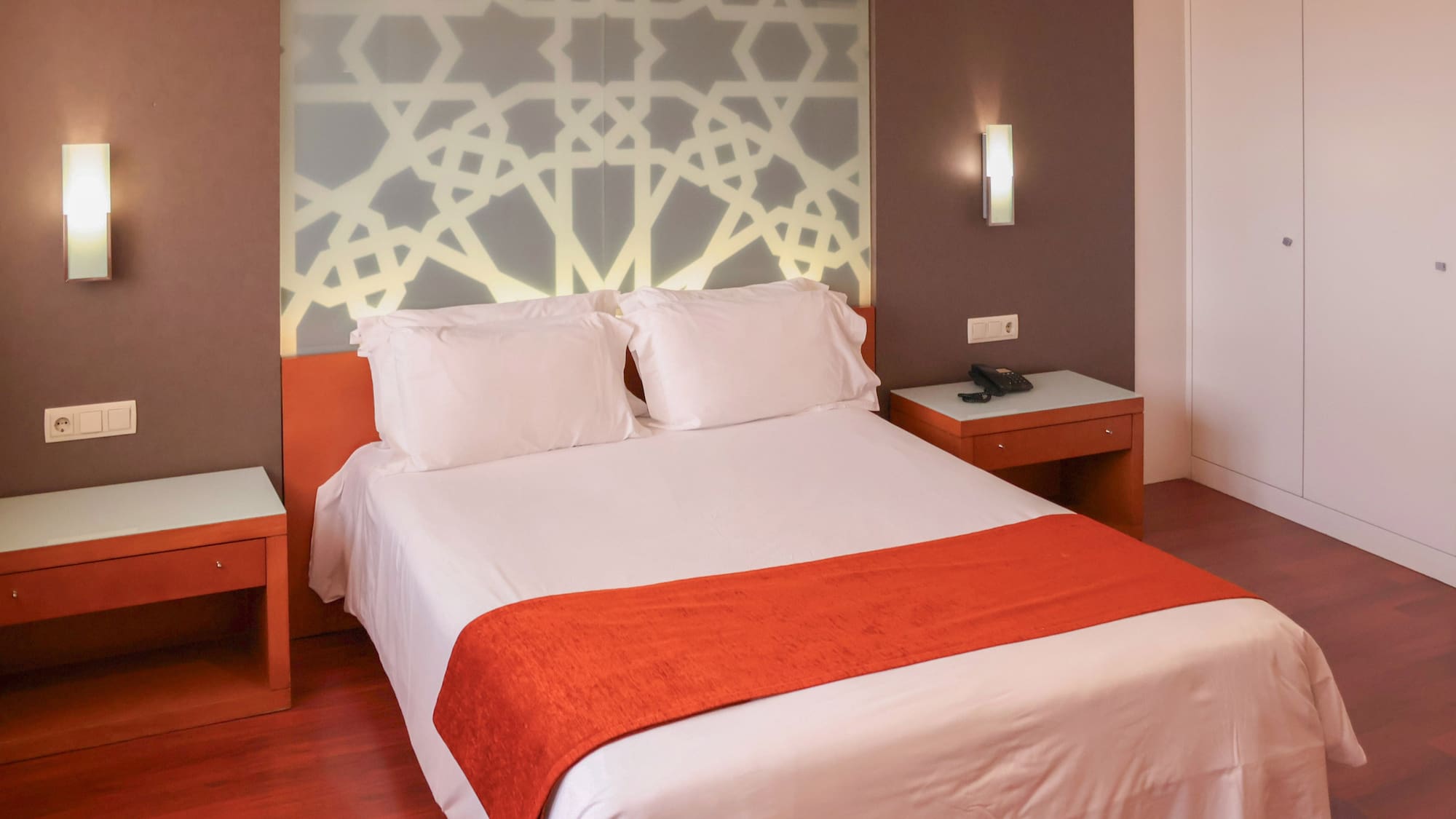 a bed with white sheets and orange blanket