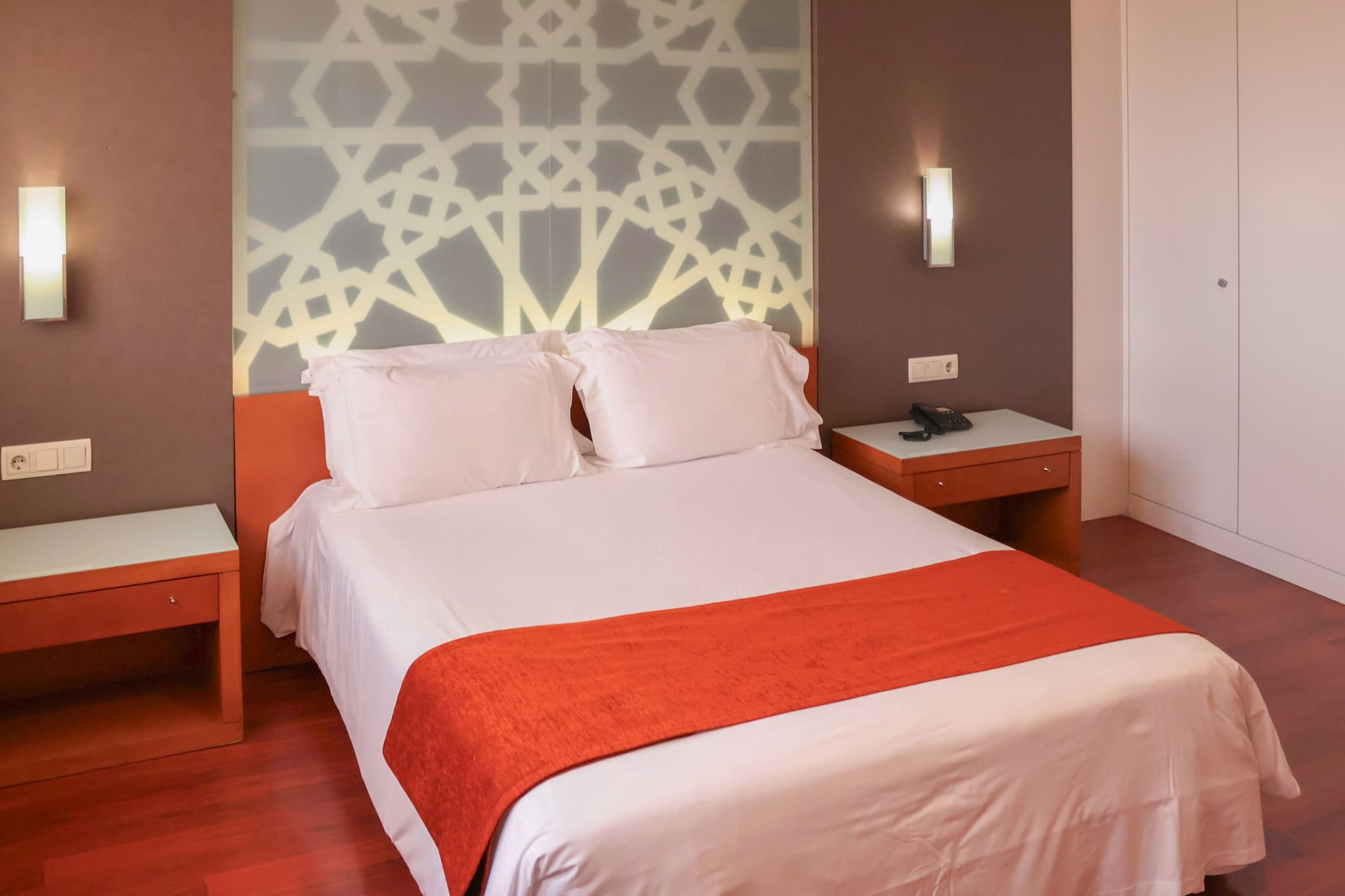 a bed with white sheets and orange blanket