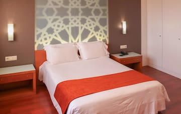 a bed with white sheets and orange blanket