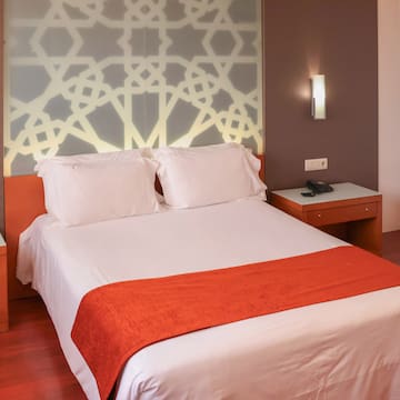 a bed with white sheets and orange blanket