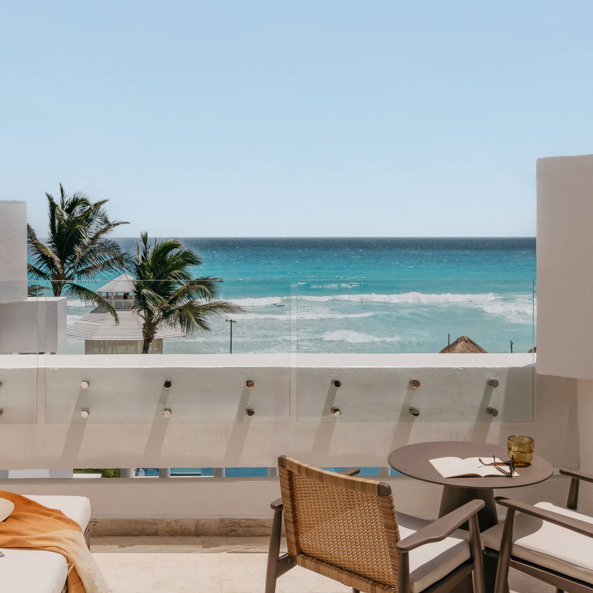 Ocean view balcony with turquoise water, palm trees, and stylish outdoor seating.