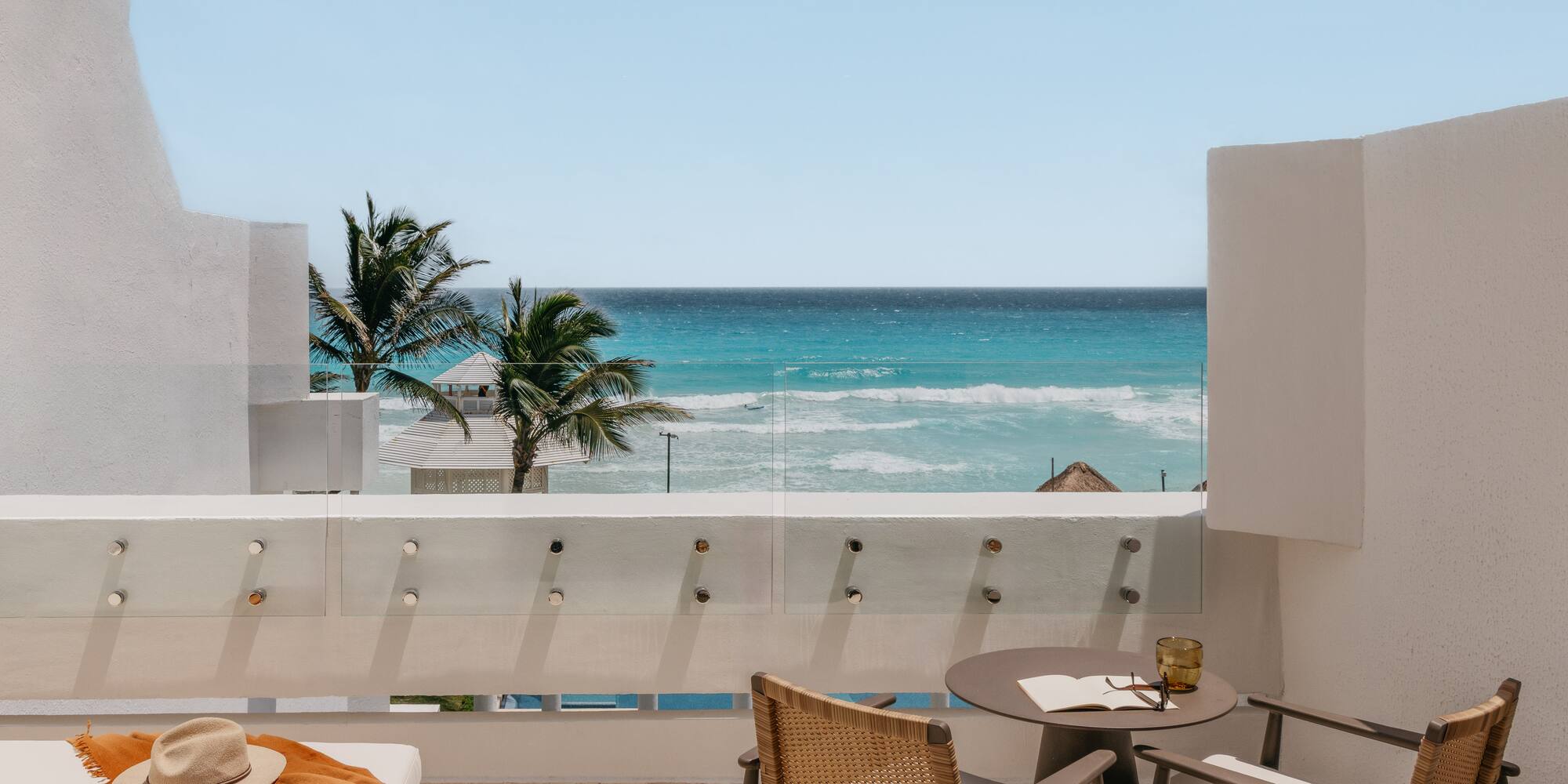 Ocean view balcony with turquoise water, palm trees, and stylish outdoor seating.
