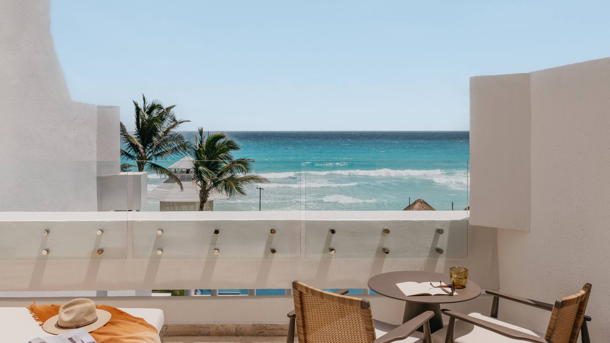 Ocean view balcony with turquoise water, palm trees, and stylish outdoor seating.