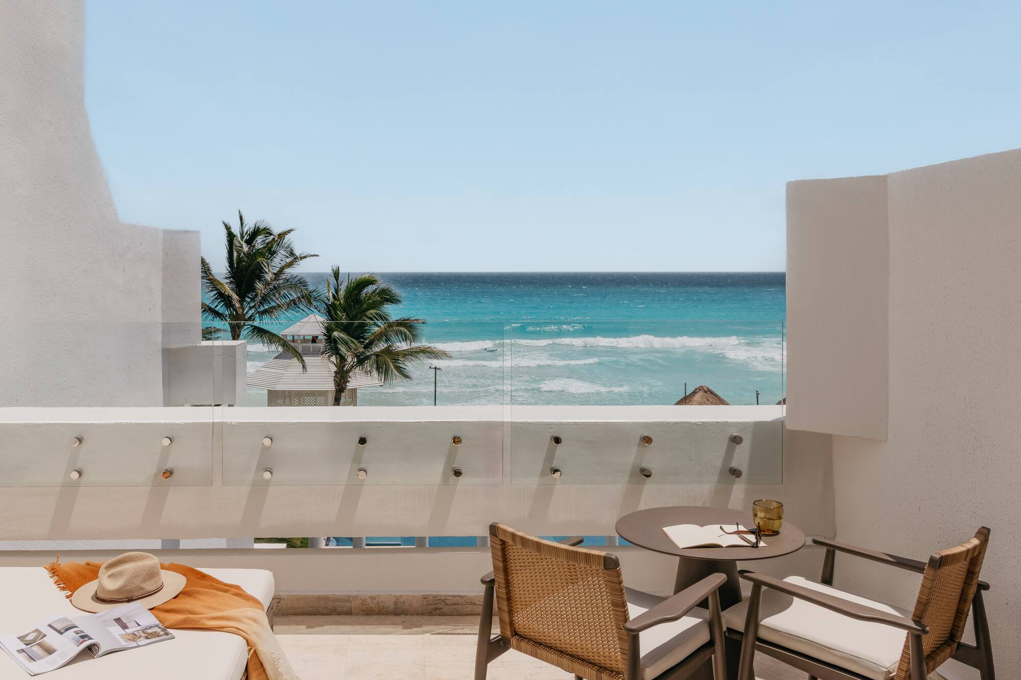 Ocean view balcony with turquoise water, palm trees, and stylish outdoor seating.