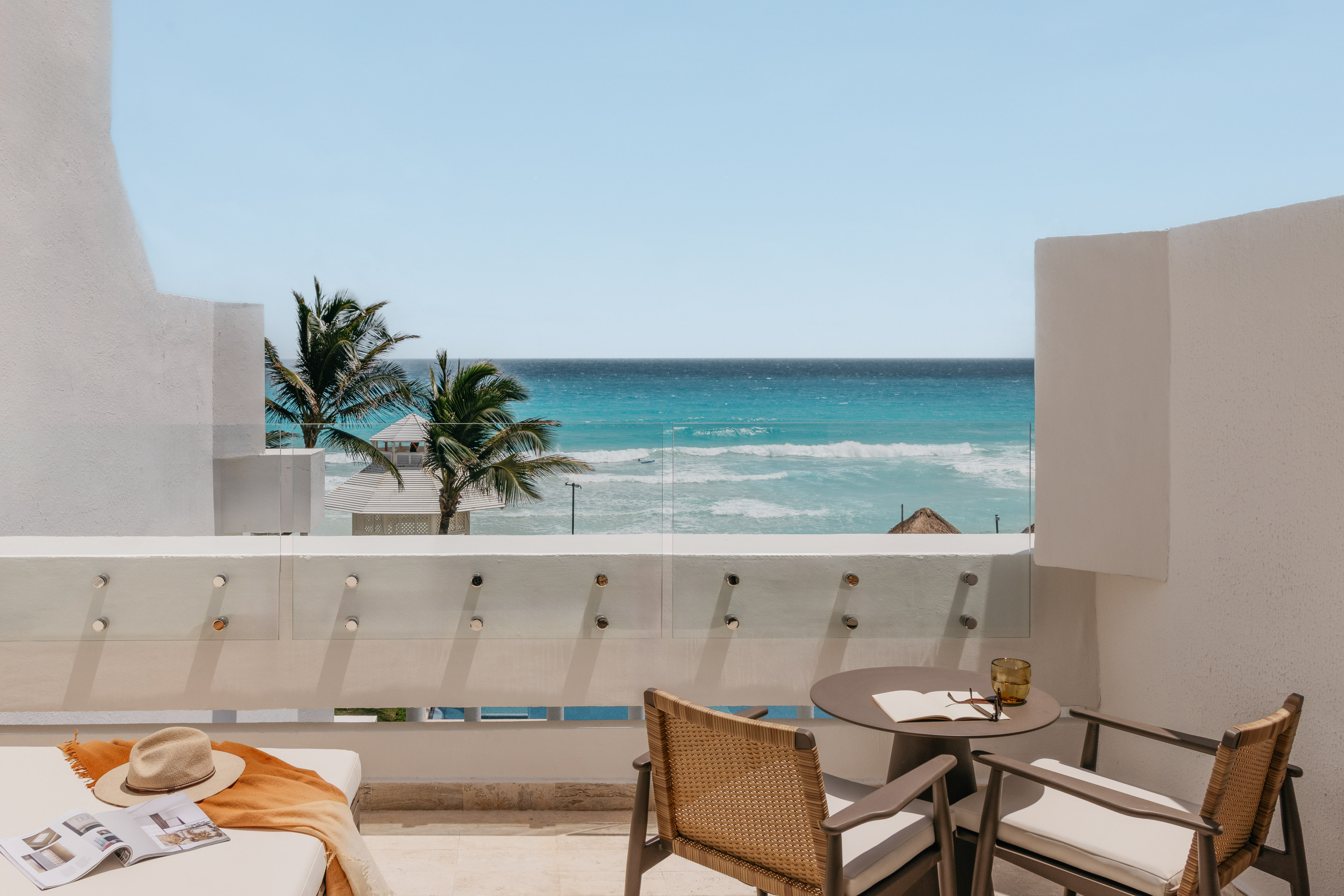 Balcony ocean view, tropical resort with palm trees and patio furniture.