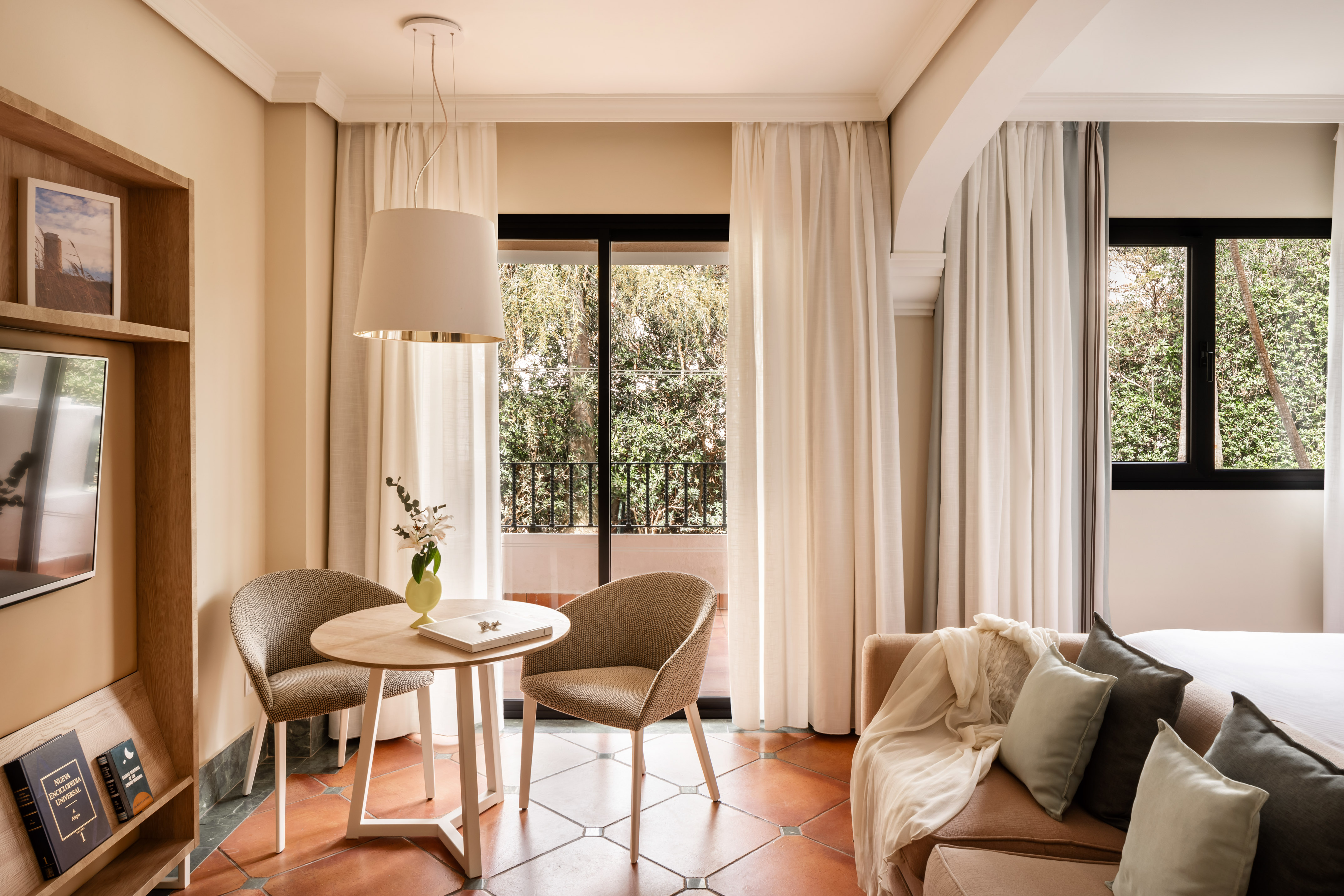 Modern hotel living area with balcony view, cozy seating, and terracotta floor.