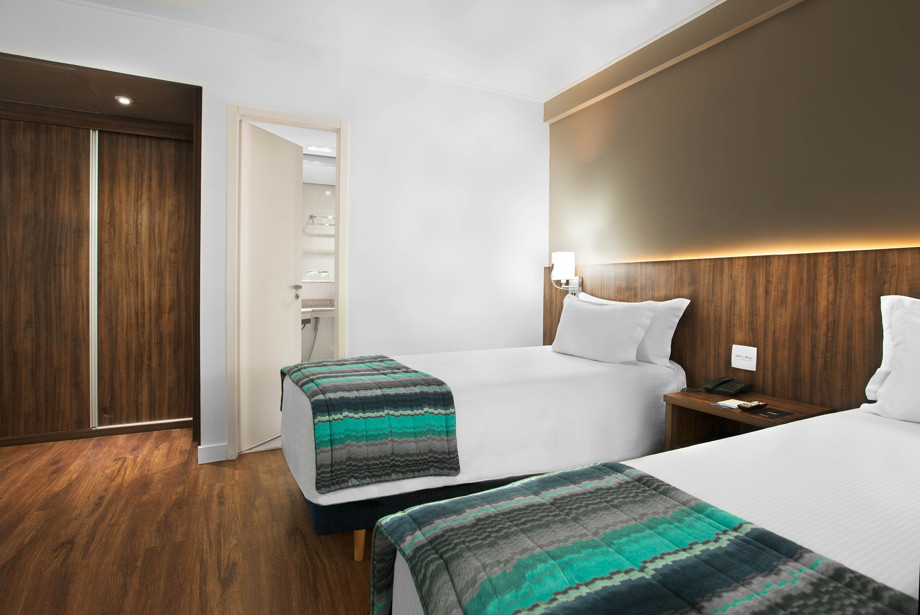 Modern hotel room with two twin beds, wood accents, and partial bathroom view.