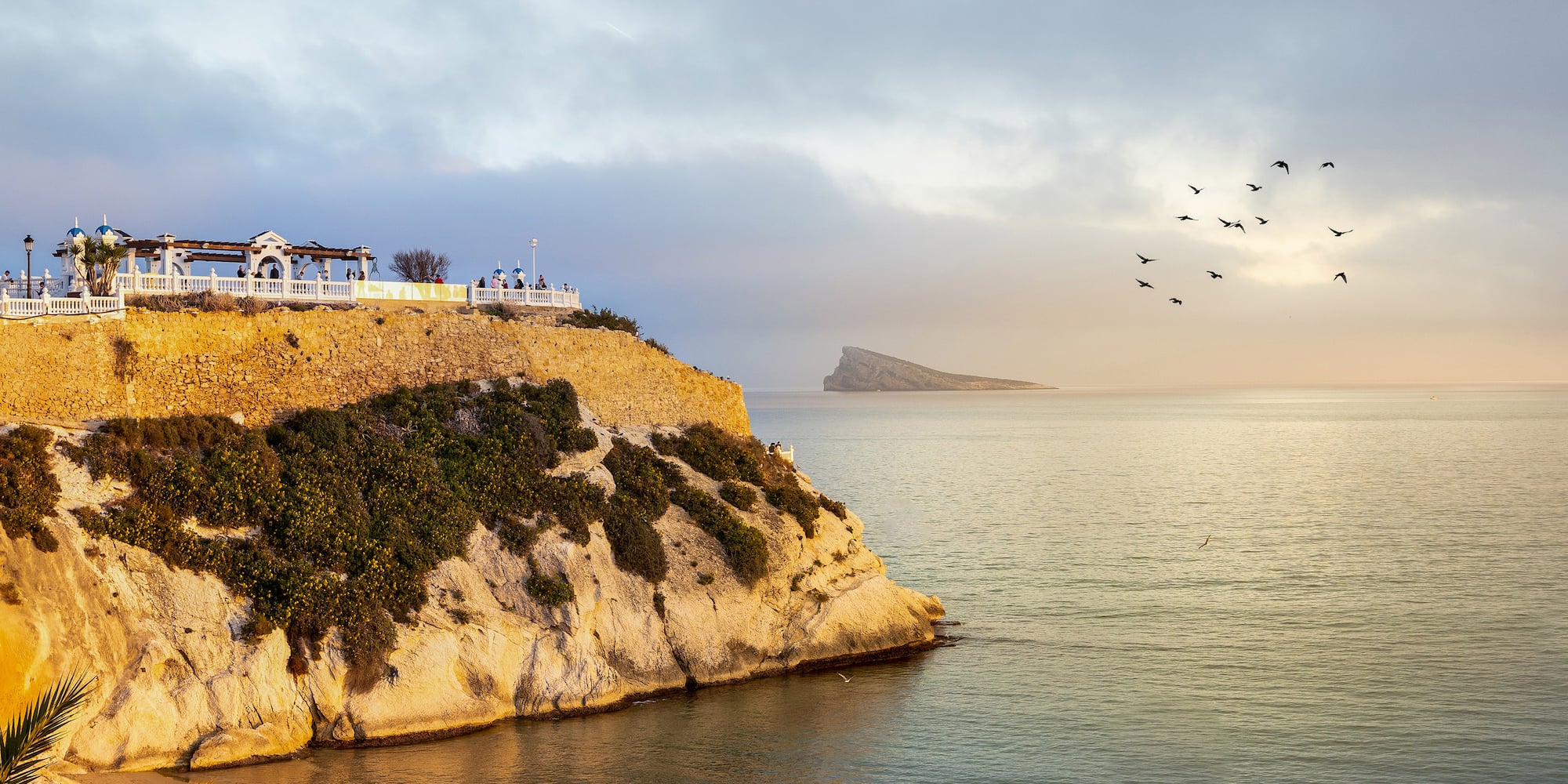 a cliff with a beach and birds flying over it