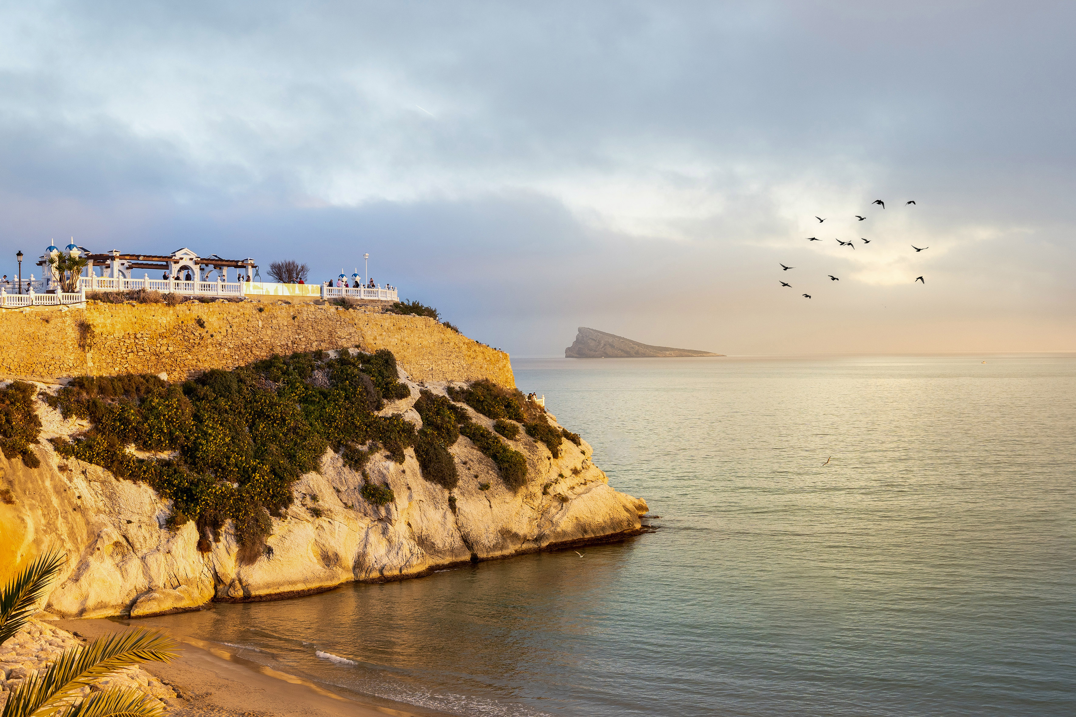 Benidorm's Balcón del Mediterráneo, sandy beach, island, and birds over the sea at dawn.
