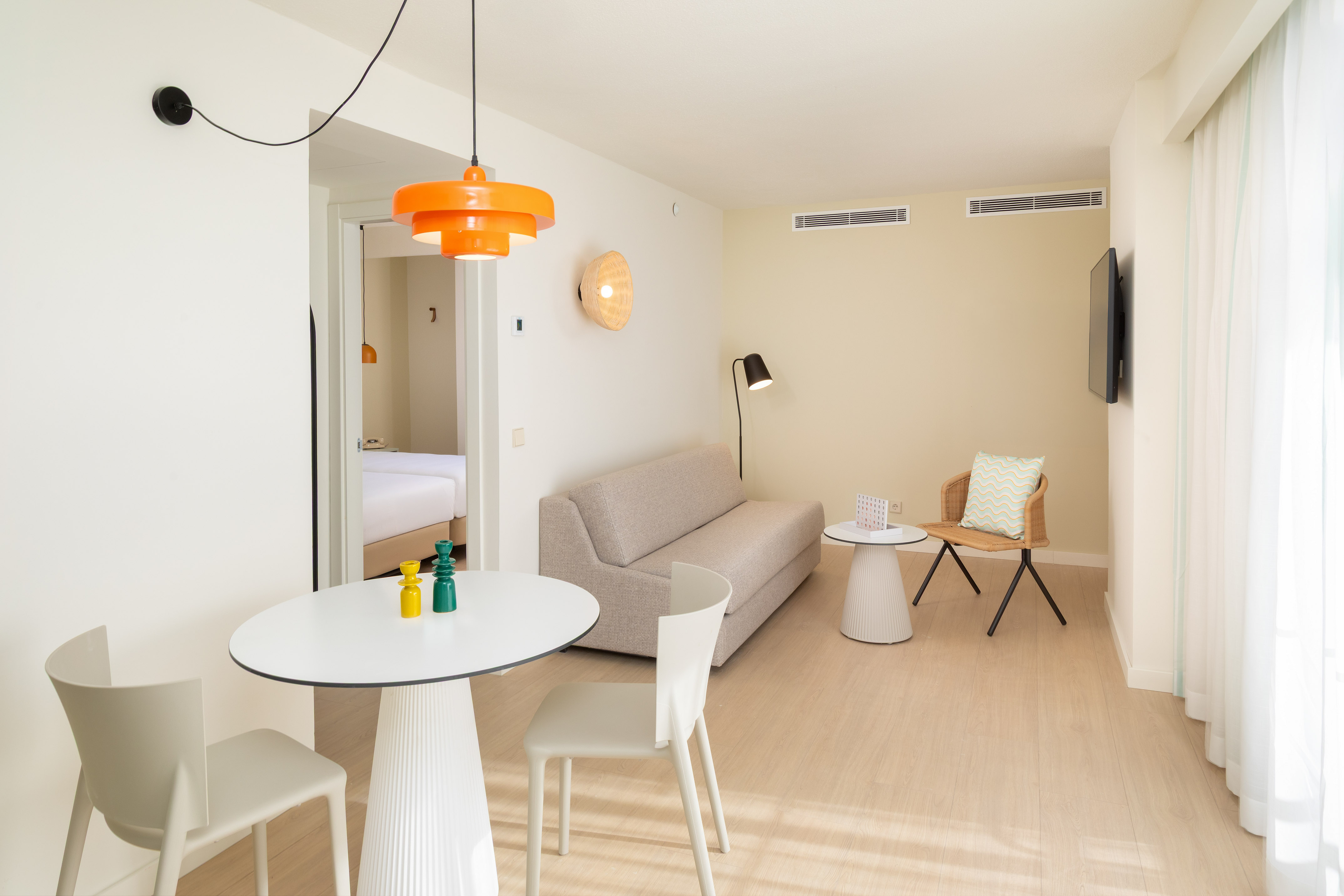 Bright hotel suite living room with modern dining, sofa, and bedroom access.