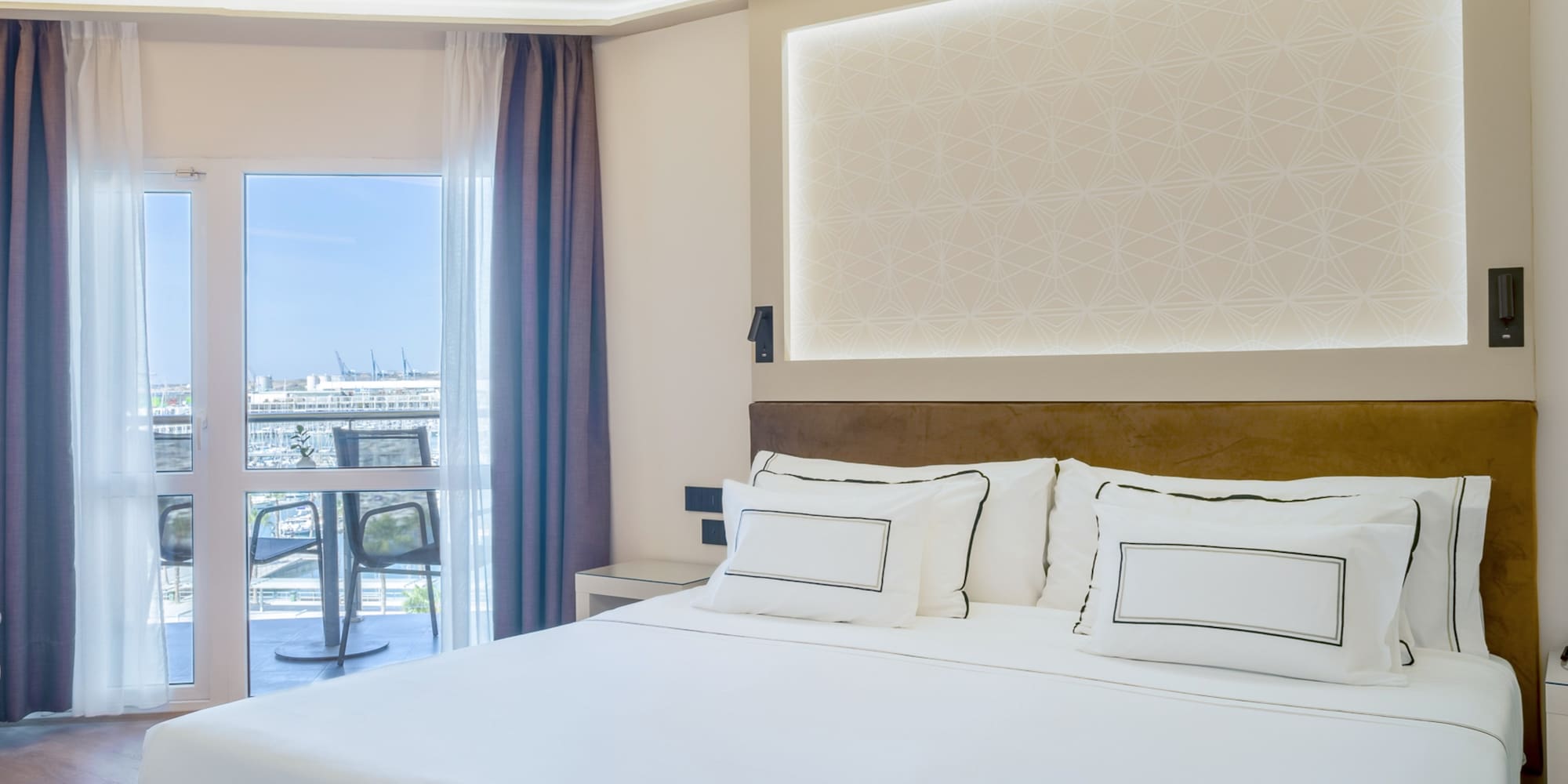 a bed with white sheets and pillows in a room with a glass door