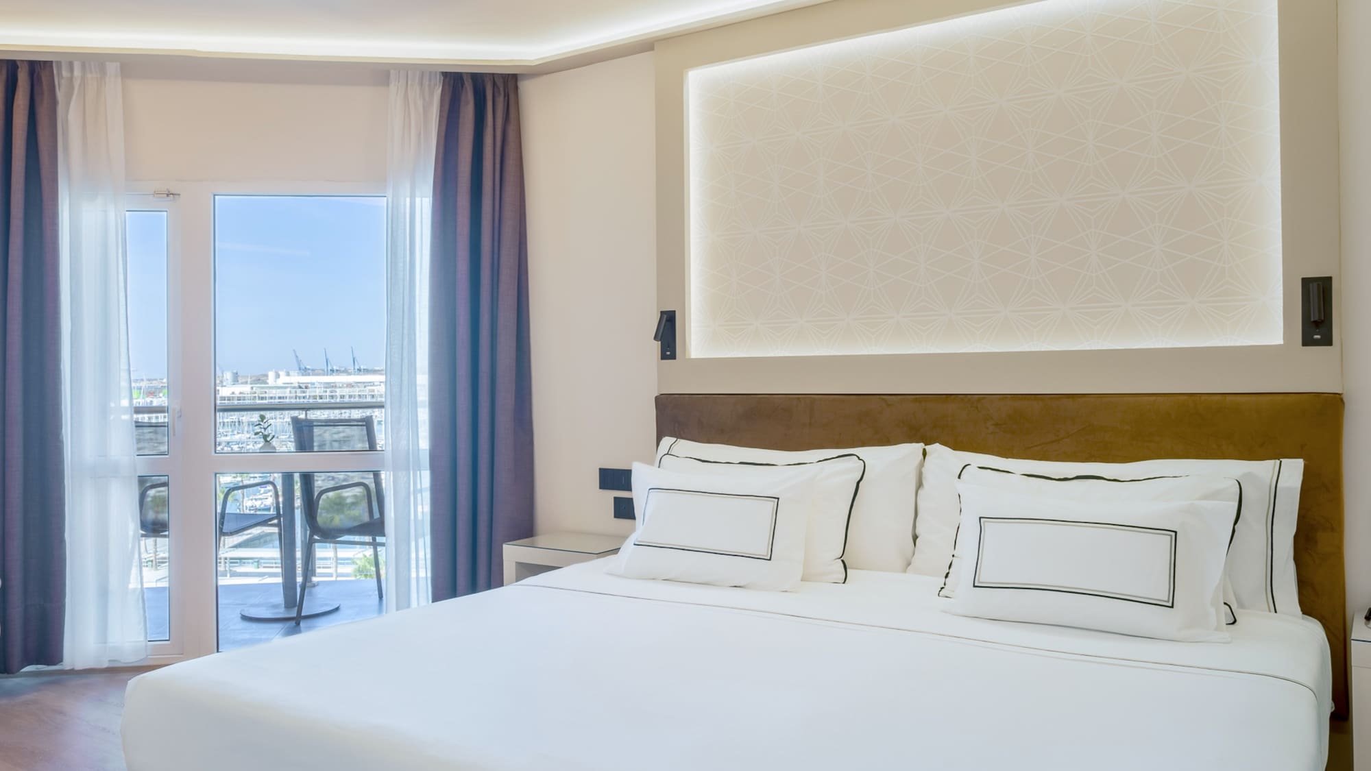 a bed with white sheets and pillows in a room with a glass door