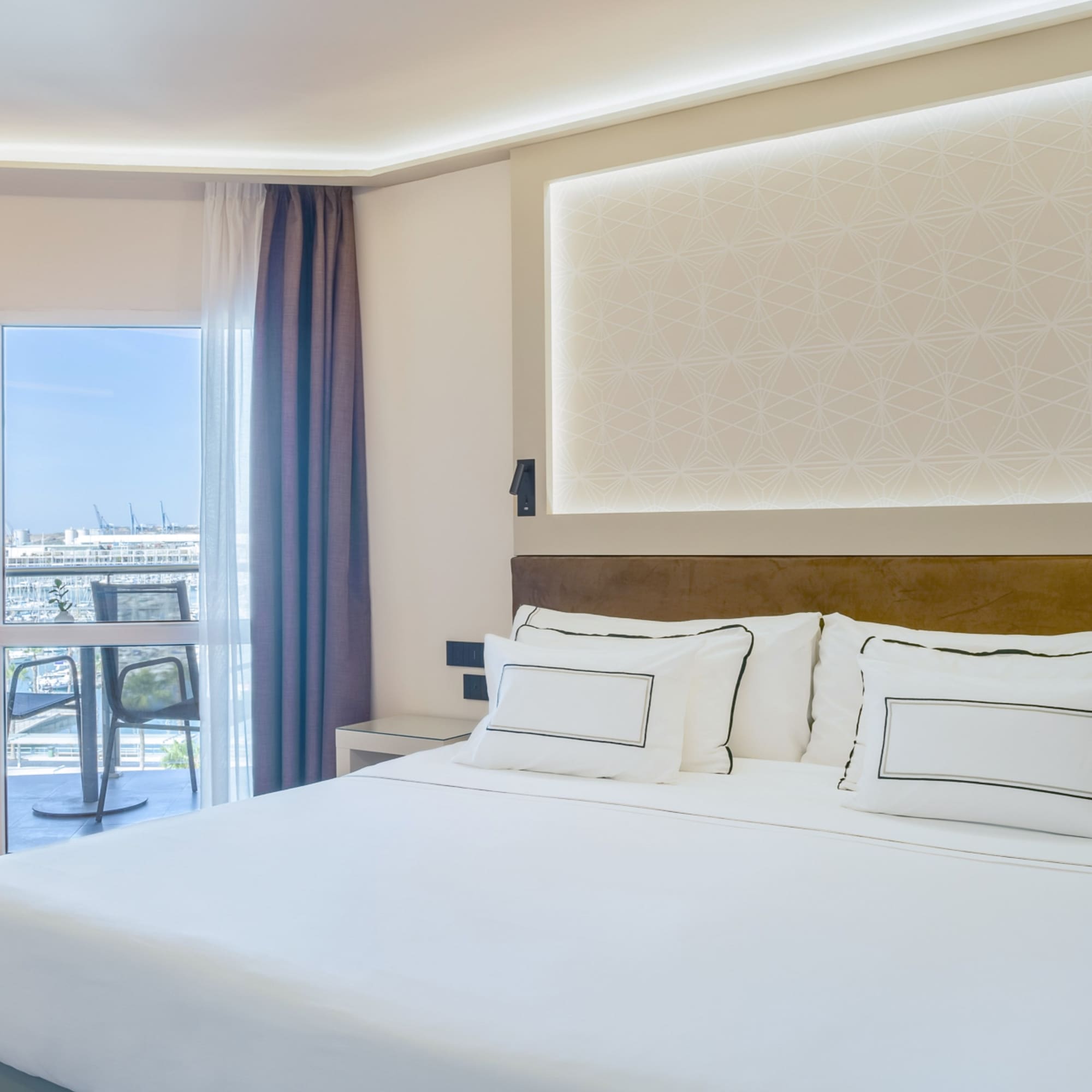 a bed with white sheets and pillows in a room with a glass door