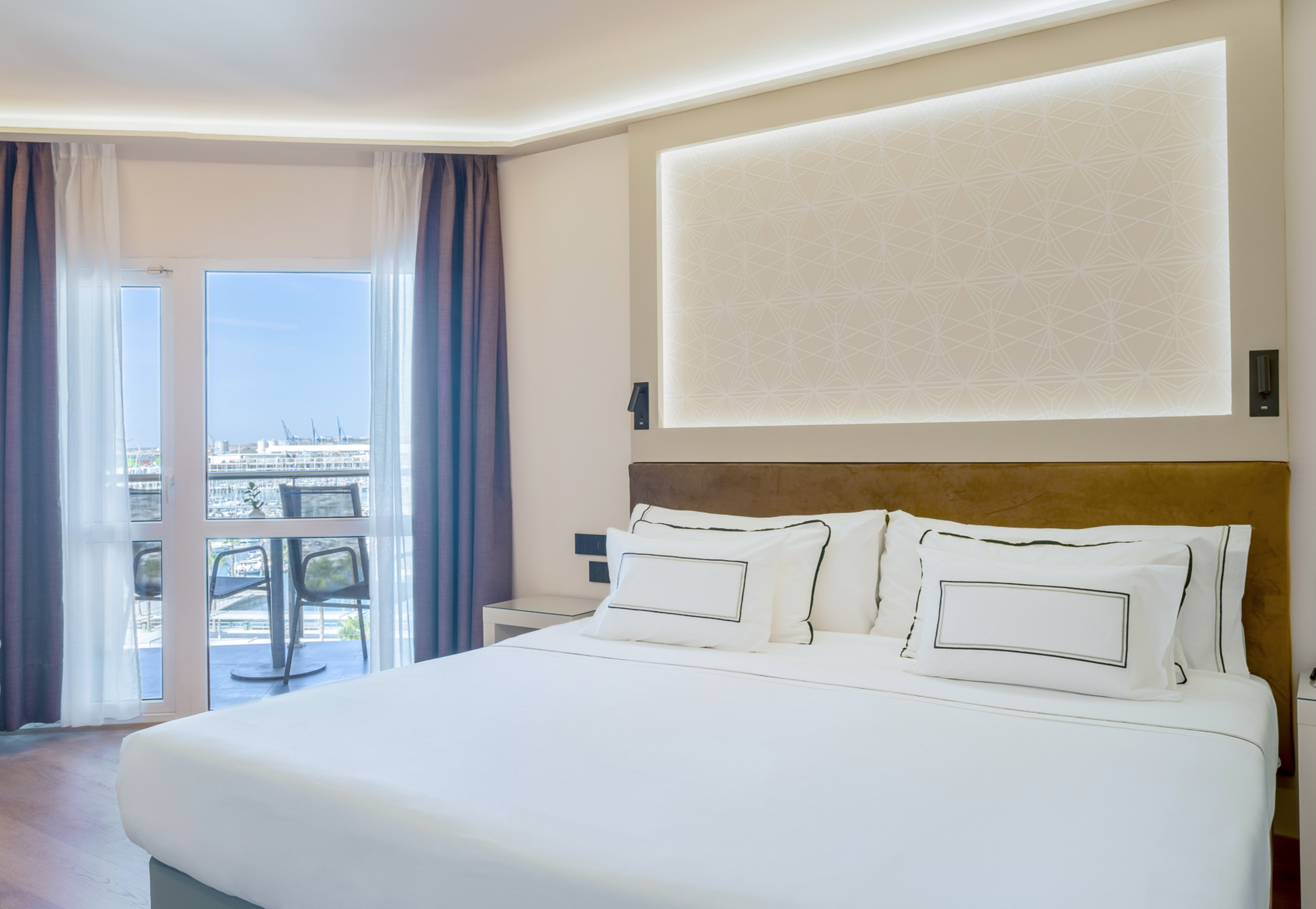 Modern hotel bedroom with white bed, balcony, and marina view.