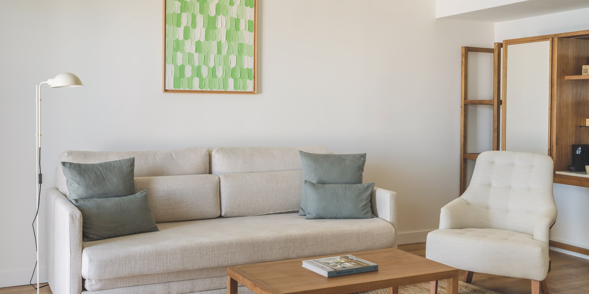 Modern living room with light sofa, armchair, wooden coffee table, green art.