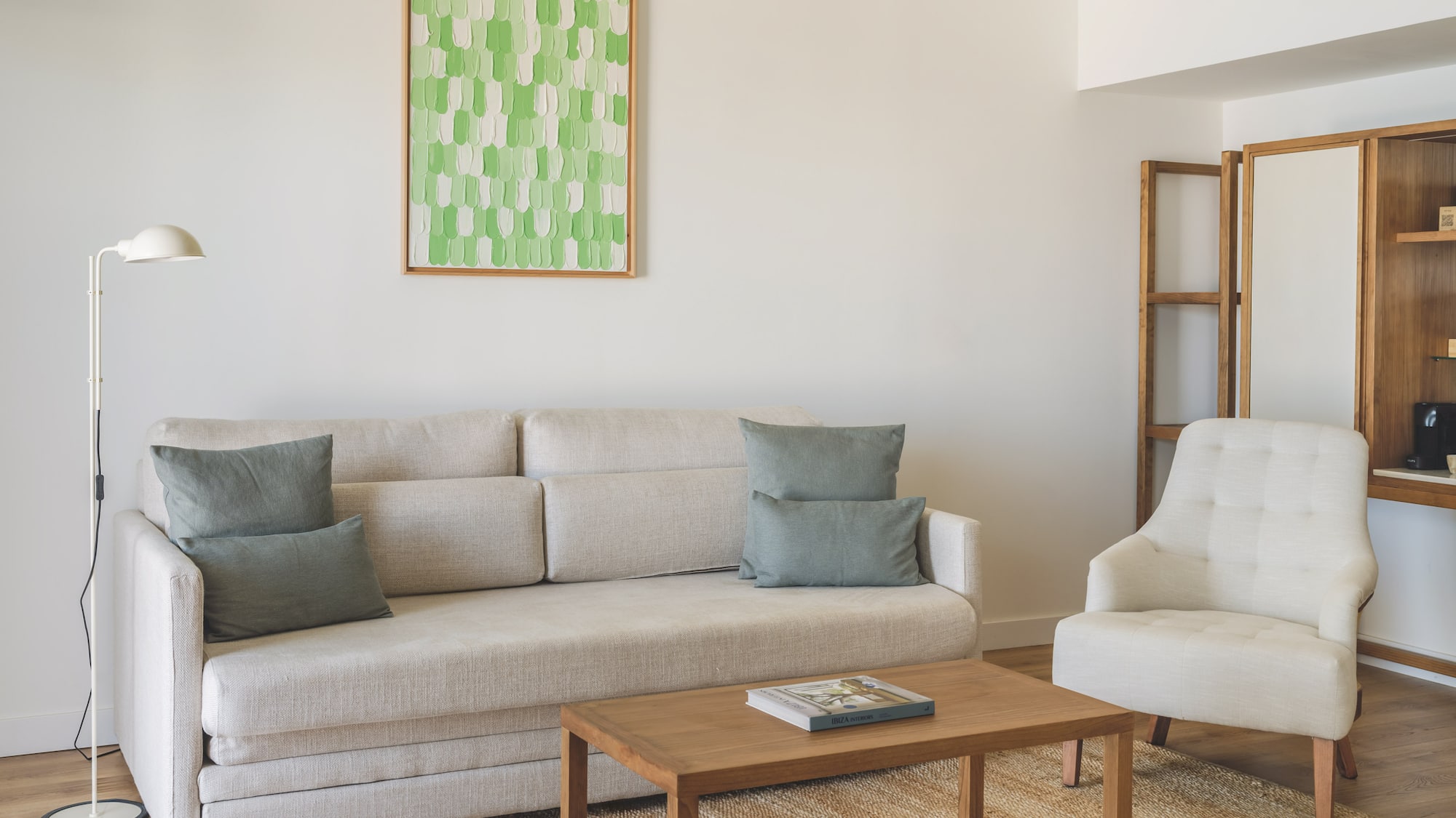 Modern living room with light sofa, armchair, wooden coffee table, green art.