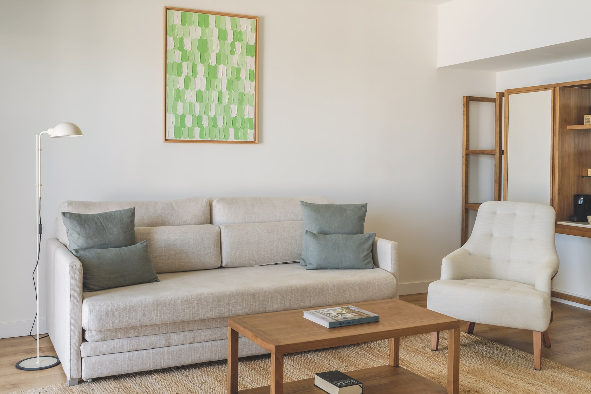 Modern living room with light sofa, armchair, wooden coffee table, green art.