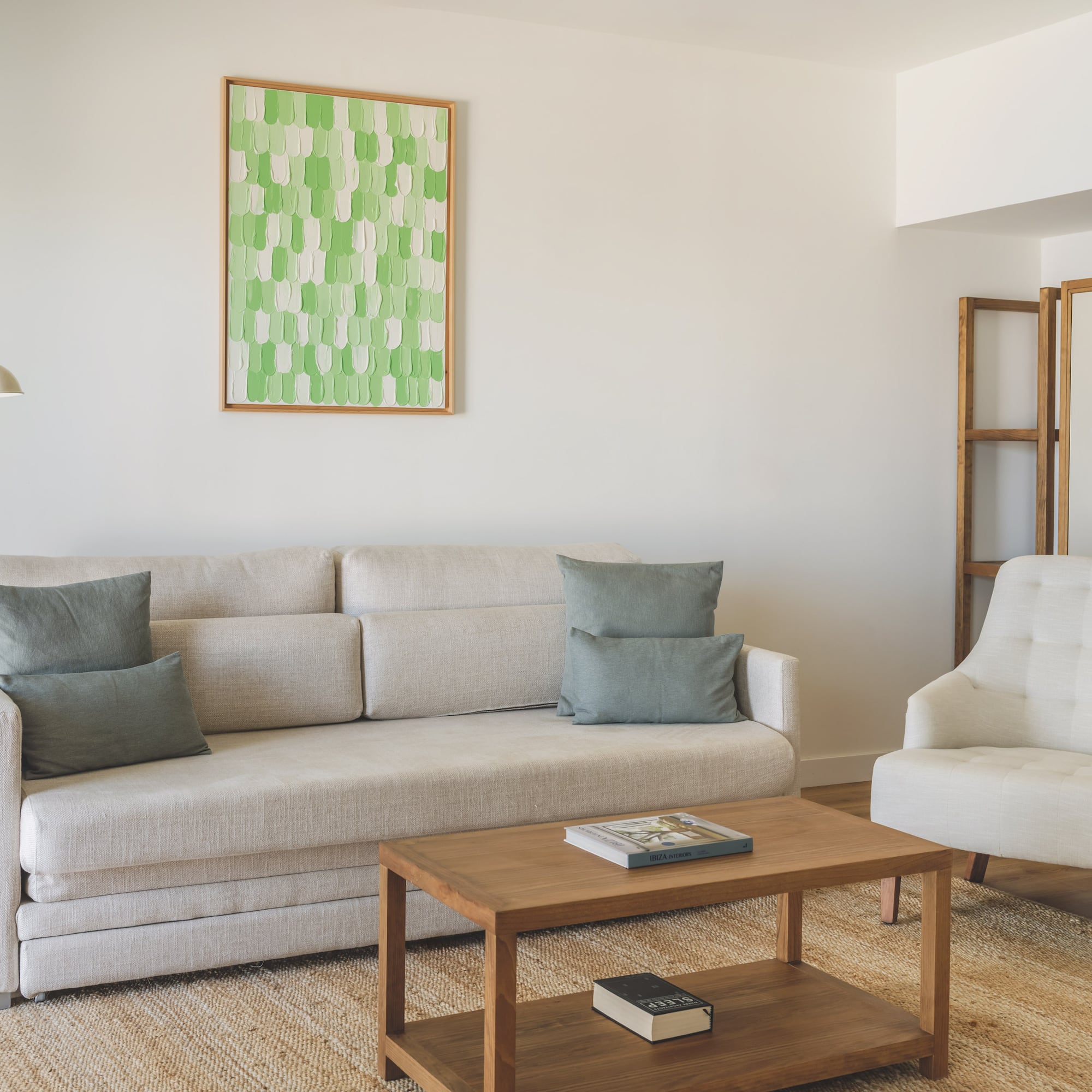 Modern living room with light sofa, armchair, wooden coffee table, green art.