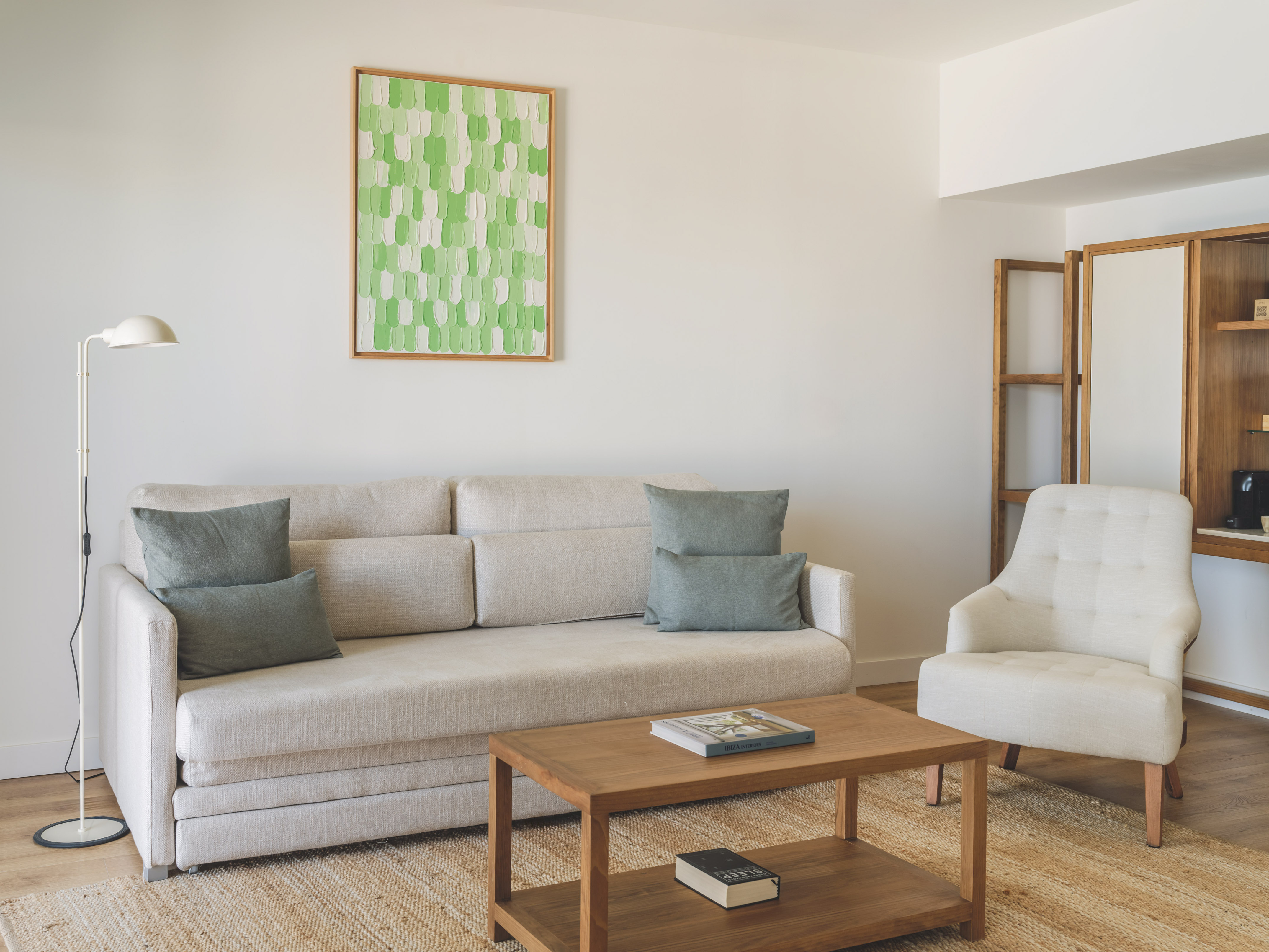Modern living room with light sofa, armchair, wooden coffee table, green art.