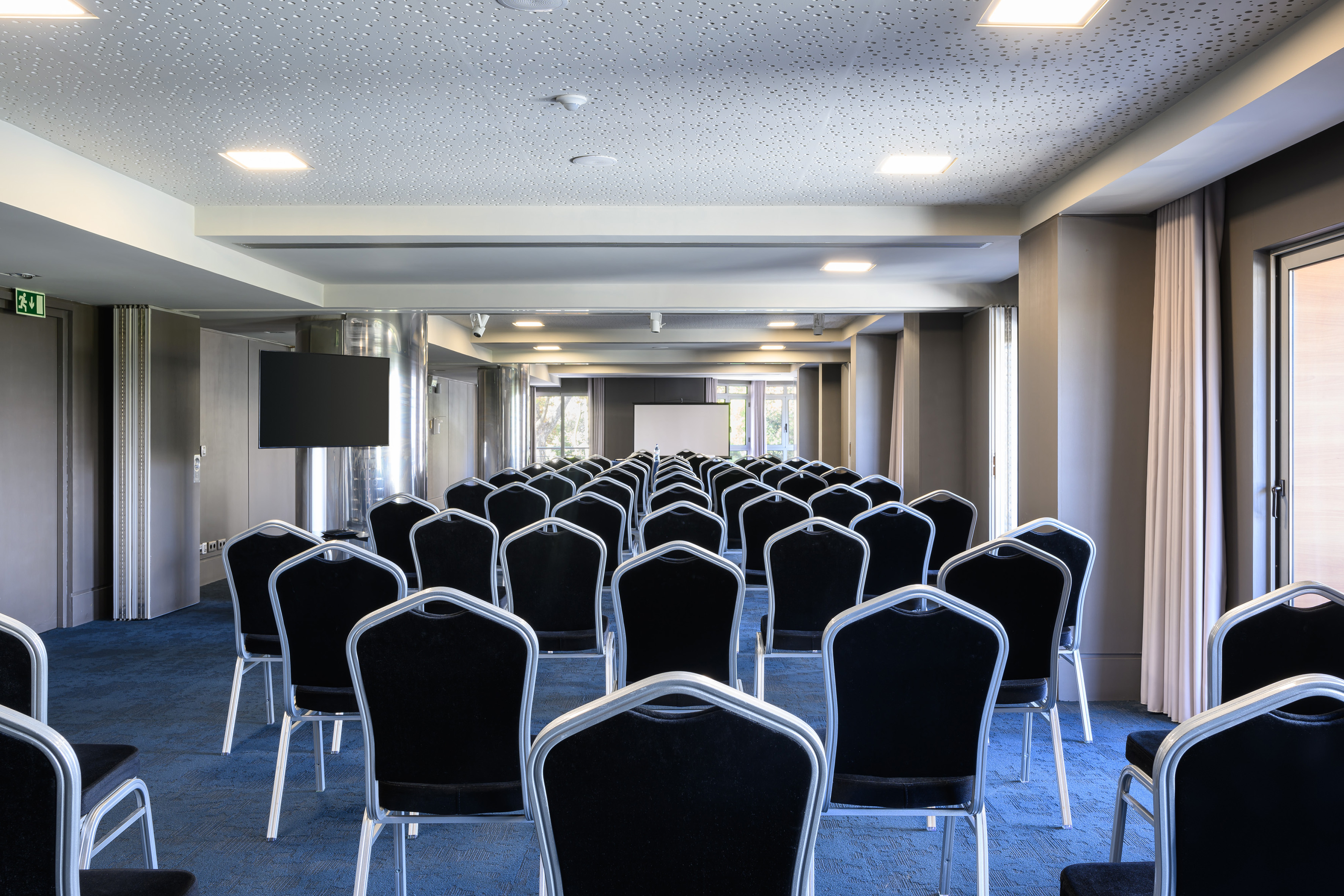 Conference room with black chairs, blue carpet, projector screen, and TV.