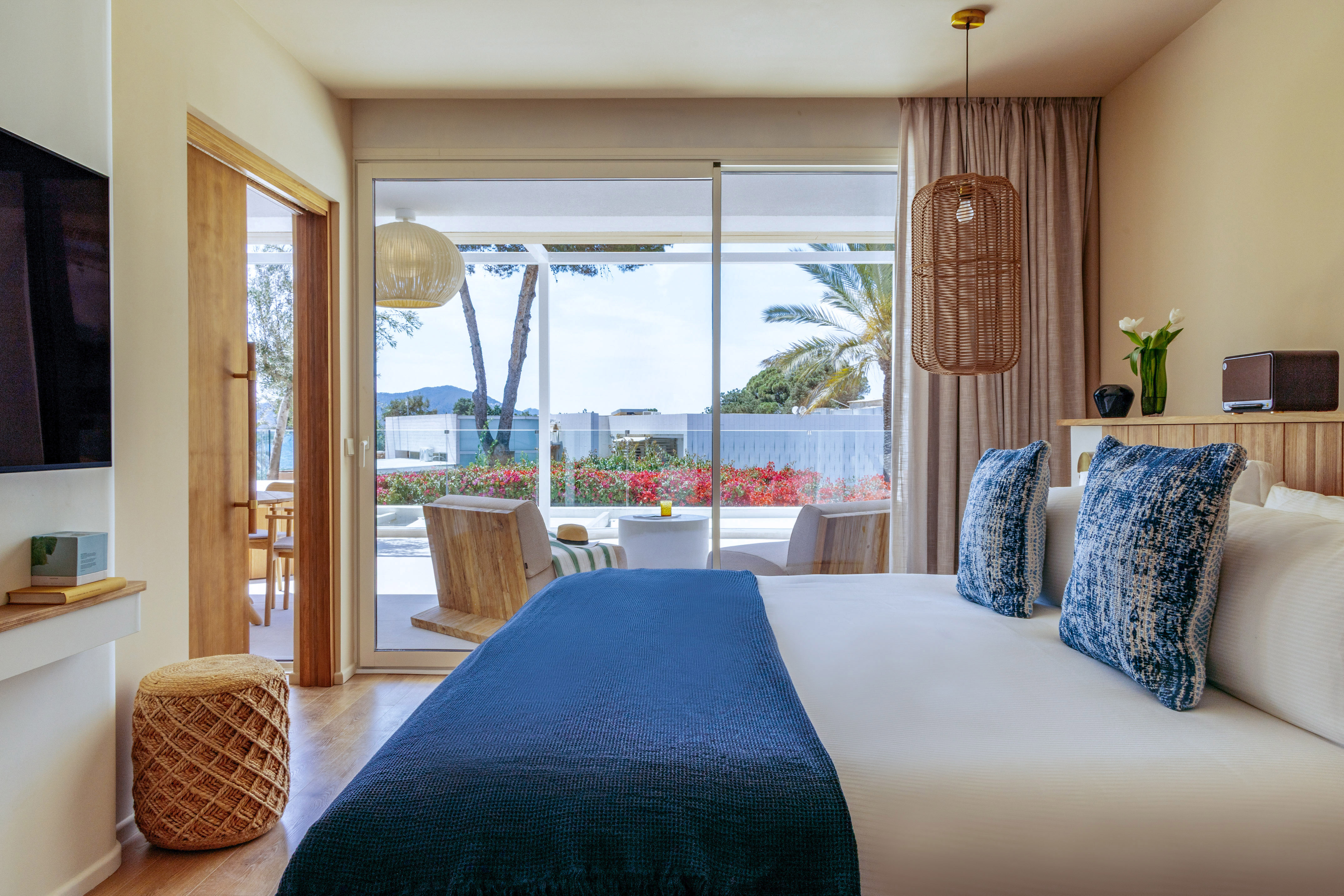 Modern hotel bedroom with blue bed, patio, and lush tropical garden view.