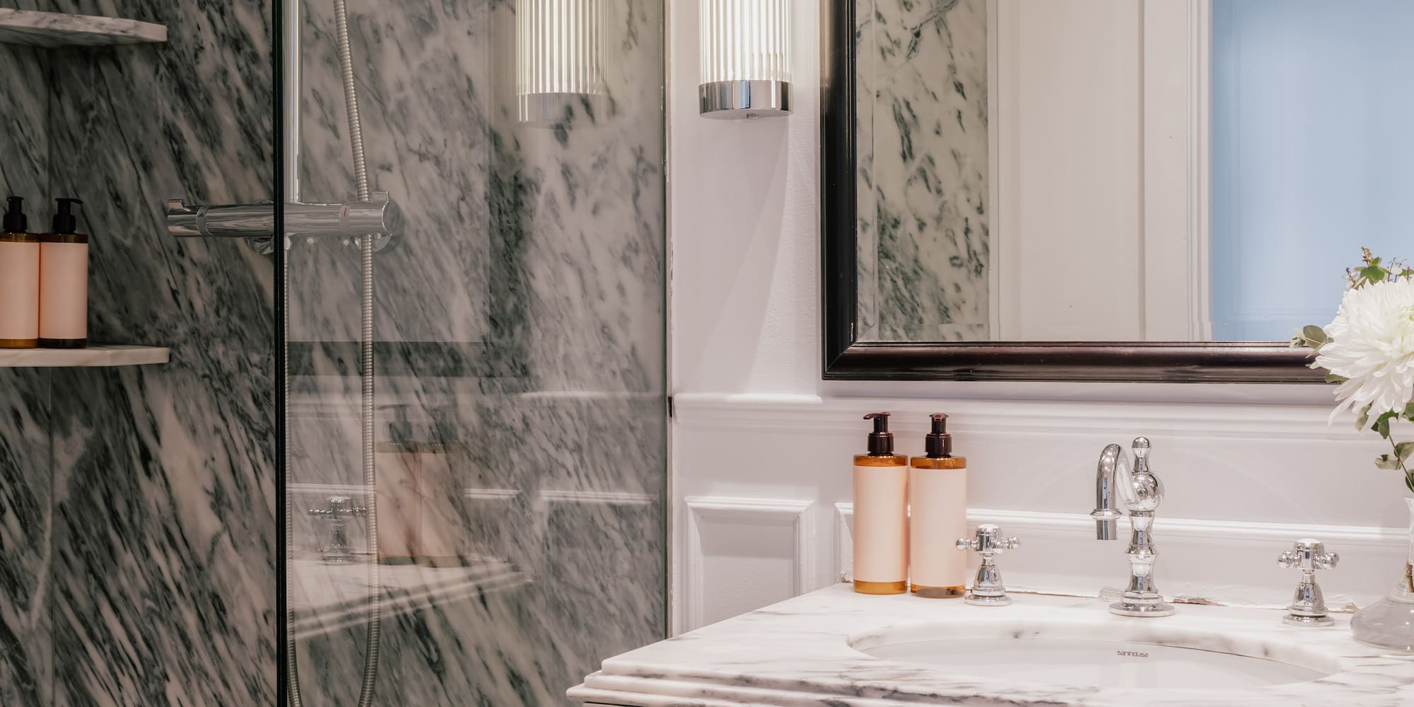 Luxury marble bathroom featuring glass shower, white vanity, mirror, and chrome details.