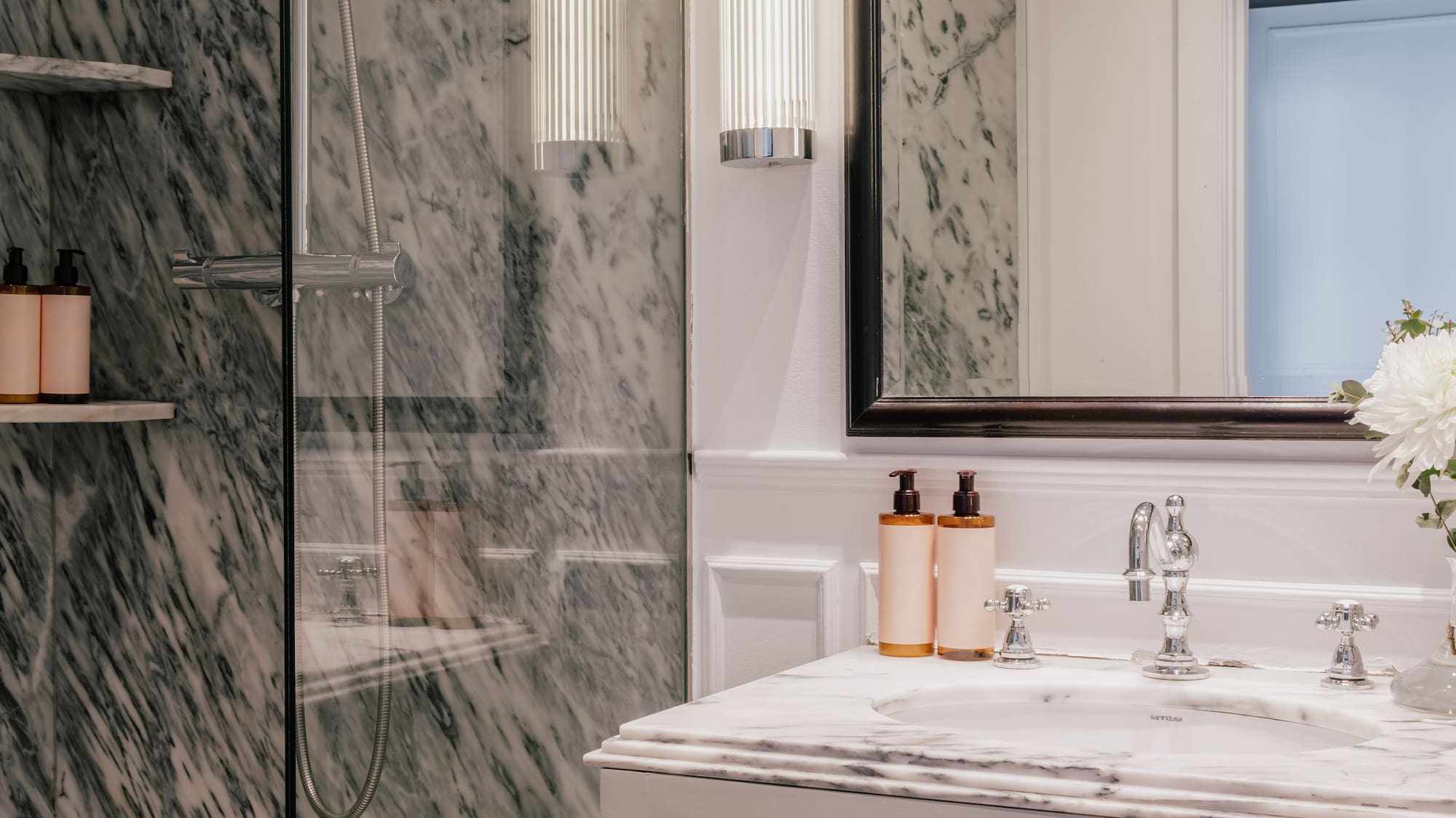 Modern marble bathroom with glass shower, vanity sink, and stylish lighting.