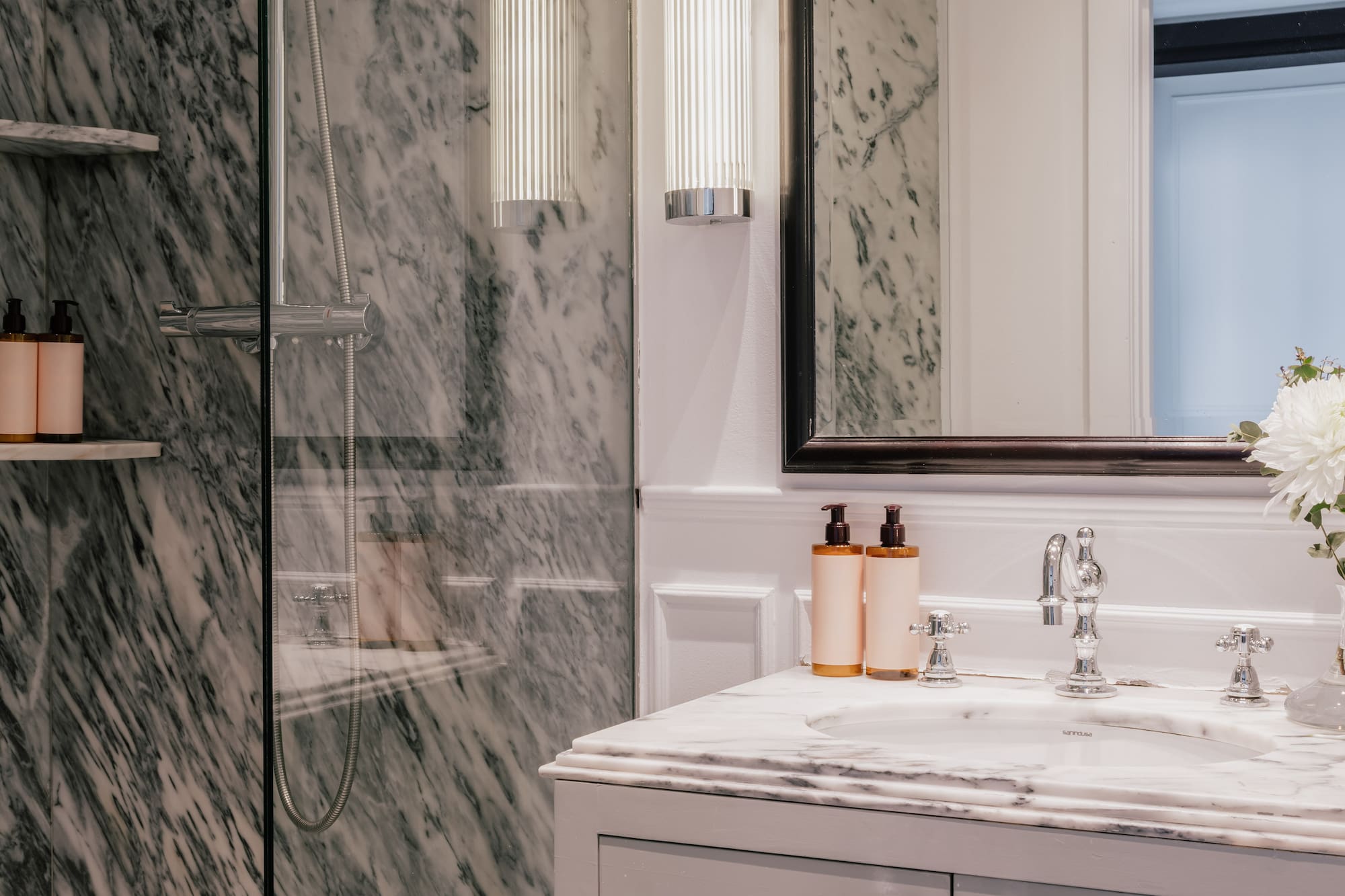 Luxury marble bathroom featuring glass shower, white vanity, mirror, and chrome details.