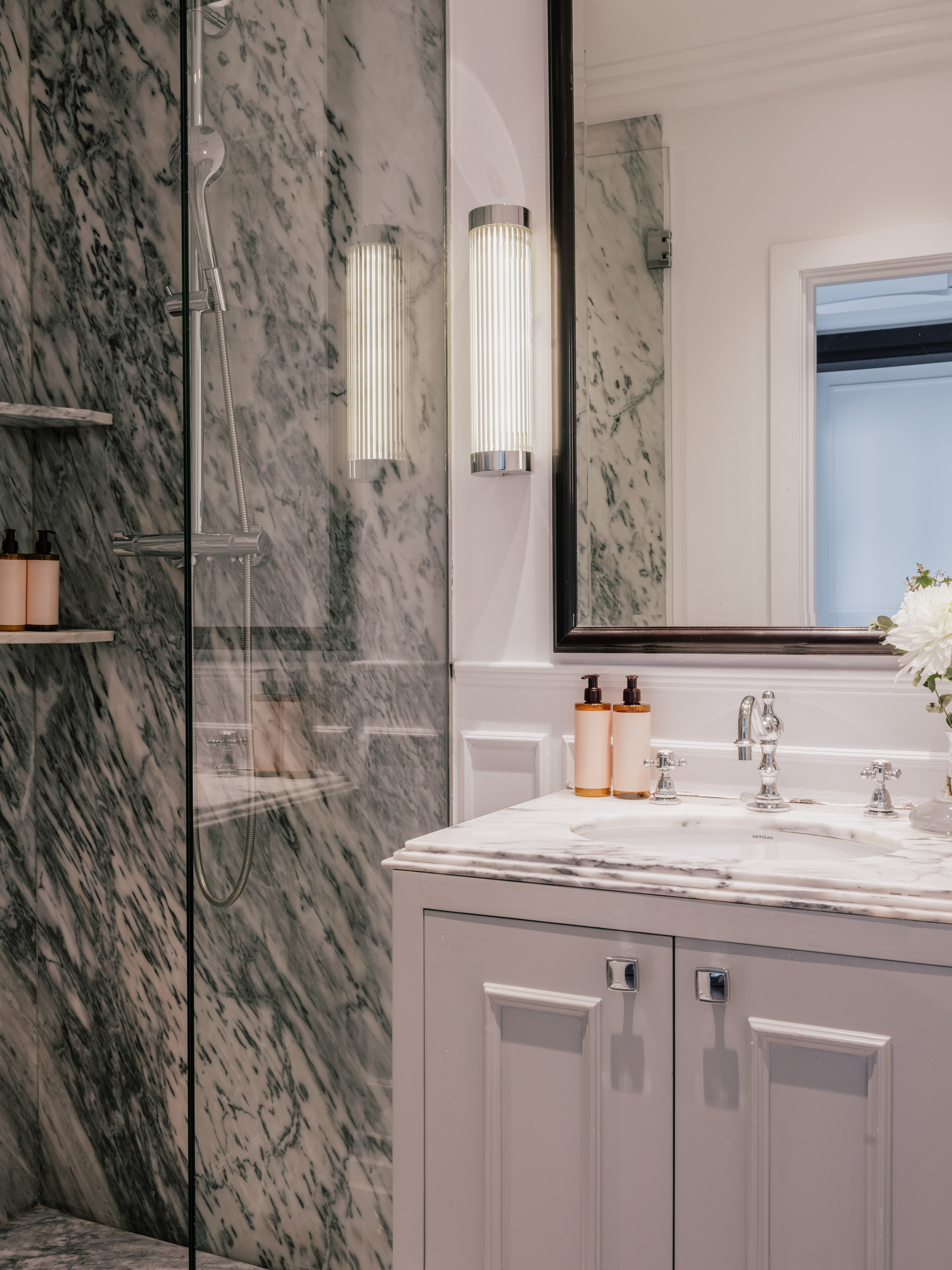 Luxury marble bathroom featuring glass shower, white vanity, mirror, and chrome details.