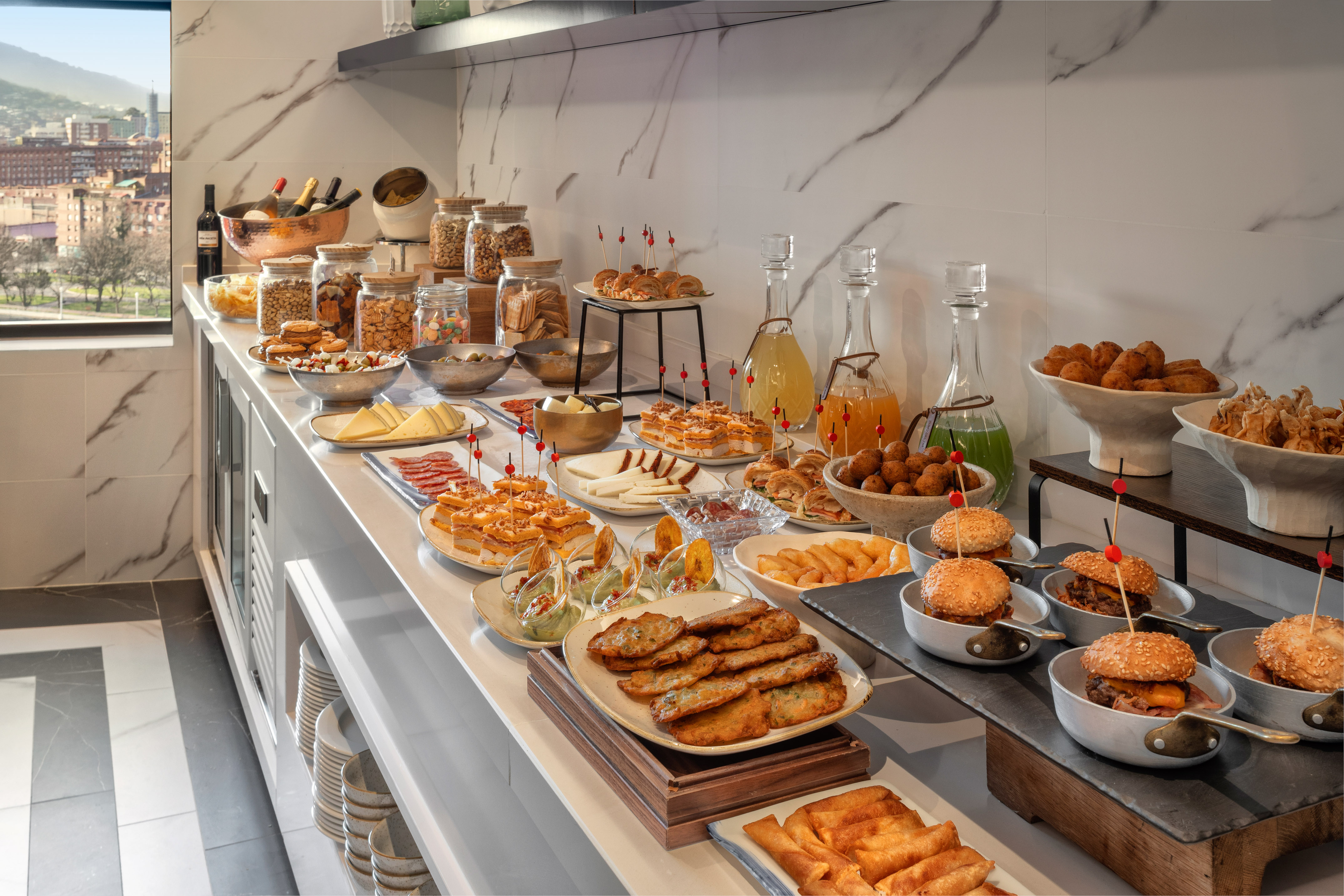 Gourmet buffet spread featuring mini burgers, tapas, cheeses, and juices.