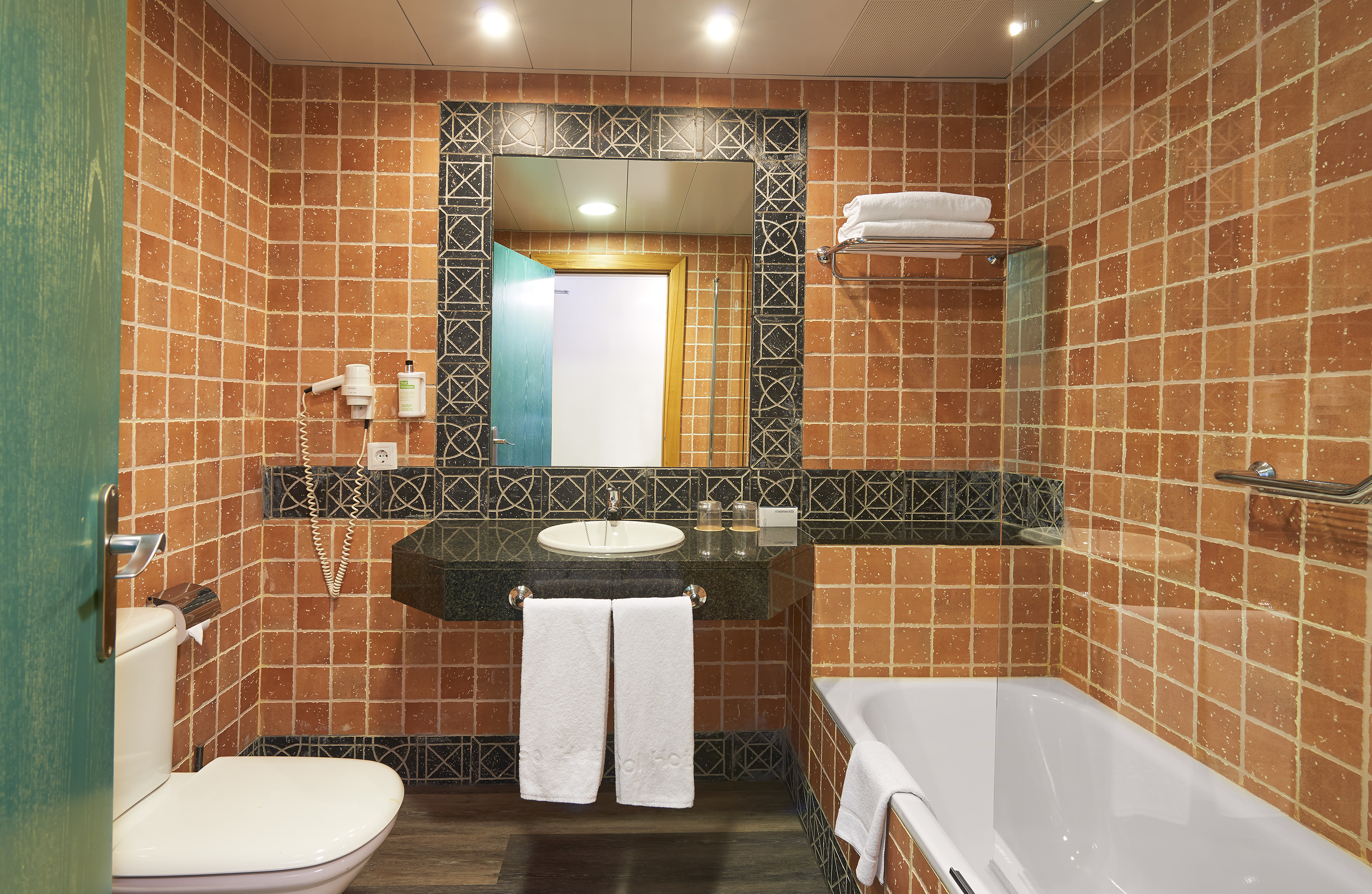 Terracotta tiled hotel bathroom with sink, mirror, toilet, and bathtub.