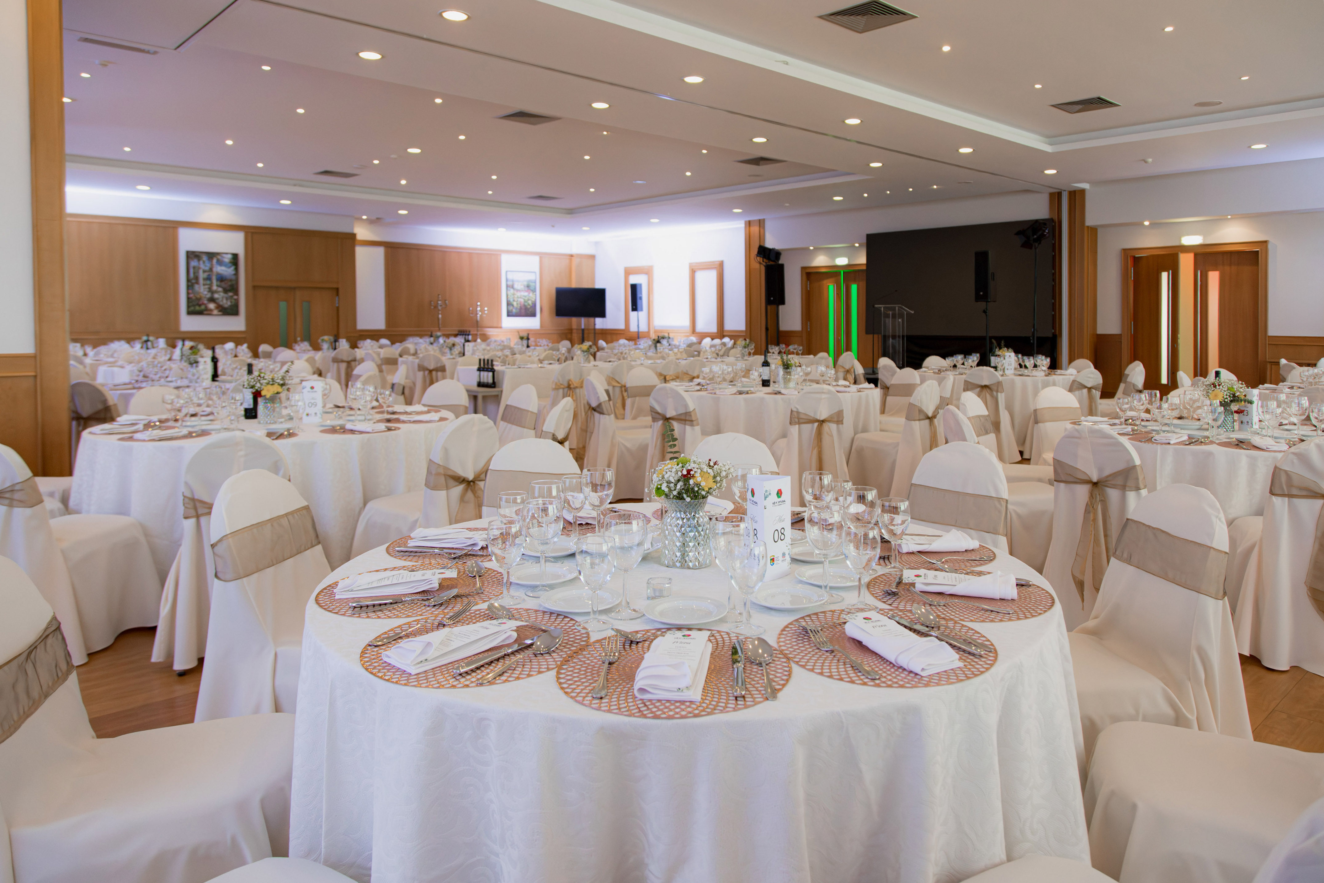 Banquet hall with elegantly set round tables, white linens, and beige chairs.