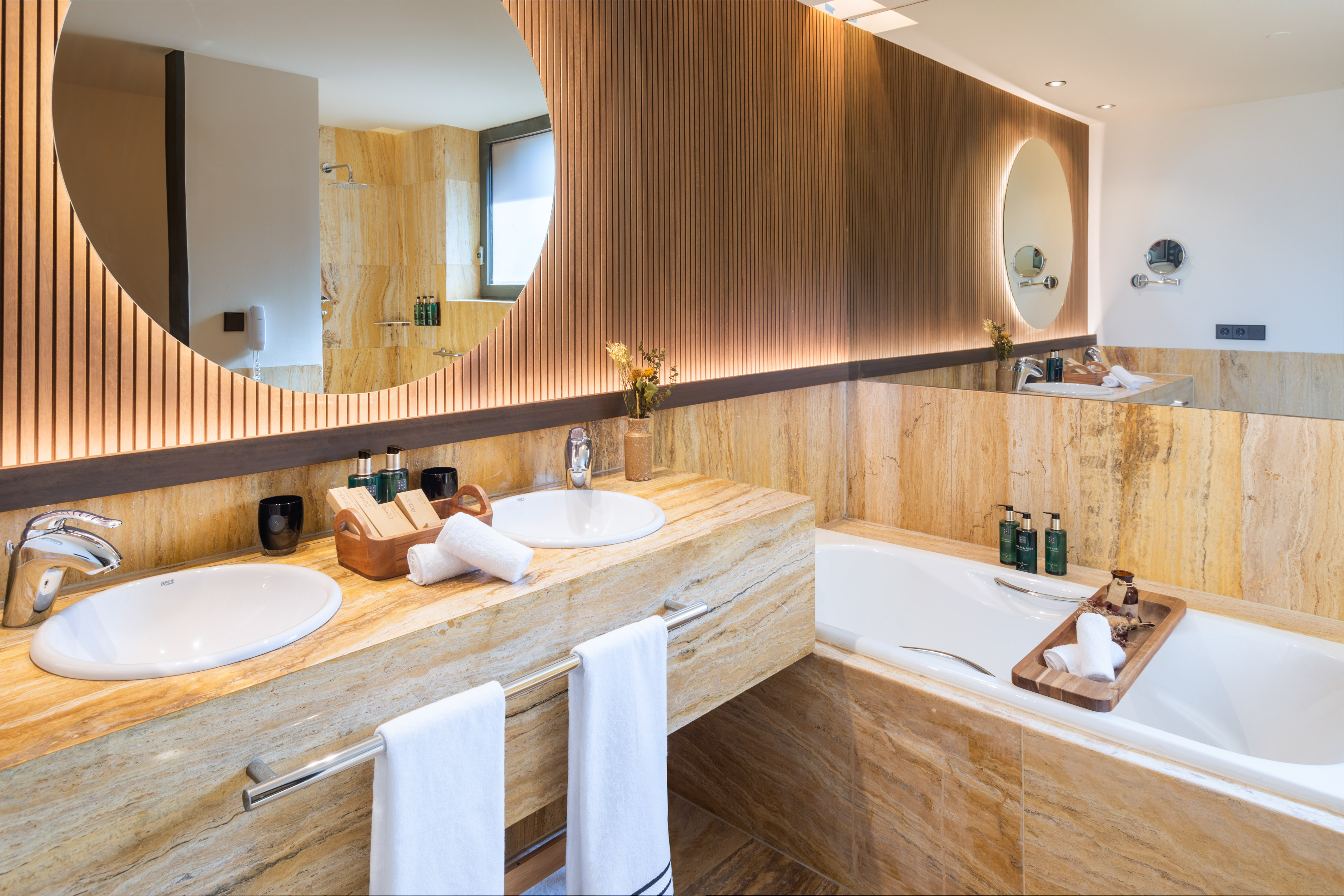 Modern bathroom with double stone vanity, wood panels, and backlit mirrors.