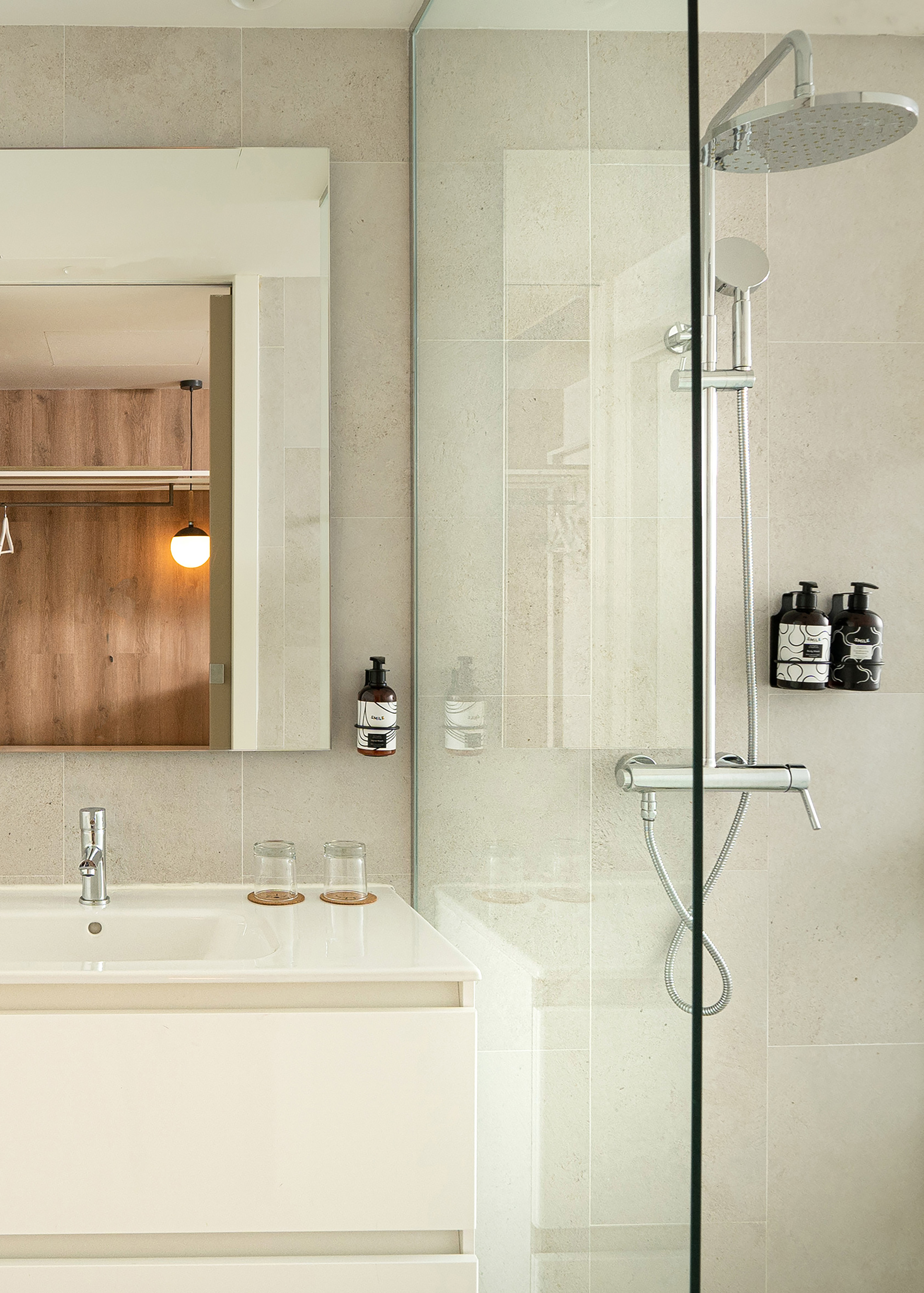 Modern bathroom with glass shower, rain head, white vanity, mirror, beige tiles.