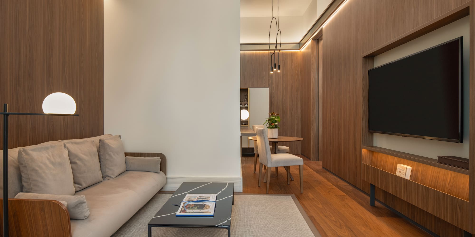 Contemporary living room with wood panels, beige sofa, coffee table, TV, and dining area.