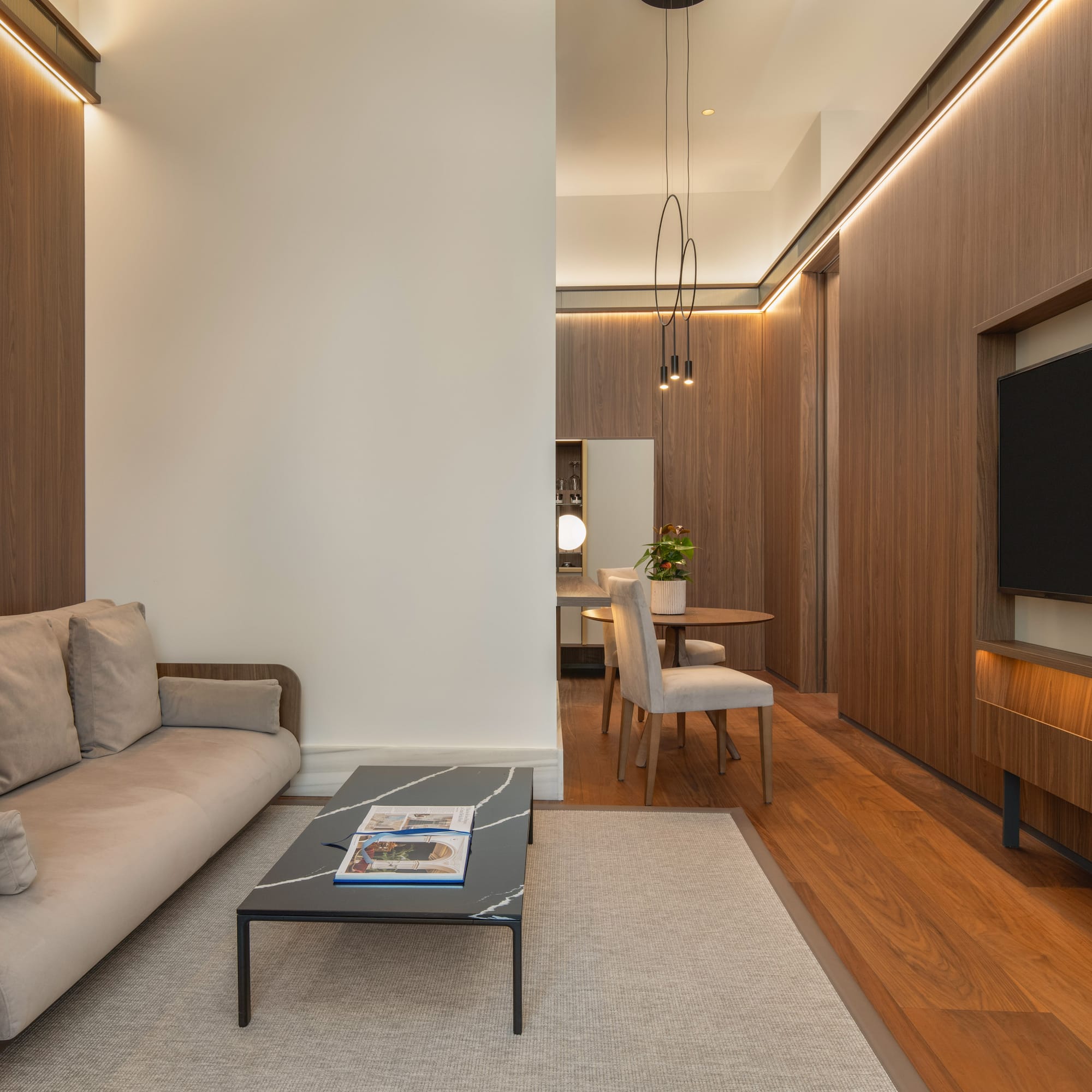 Contemporary living room with wood panels, beige sofa, coffee table, TV, and dining area.