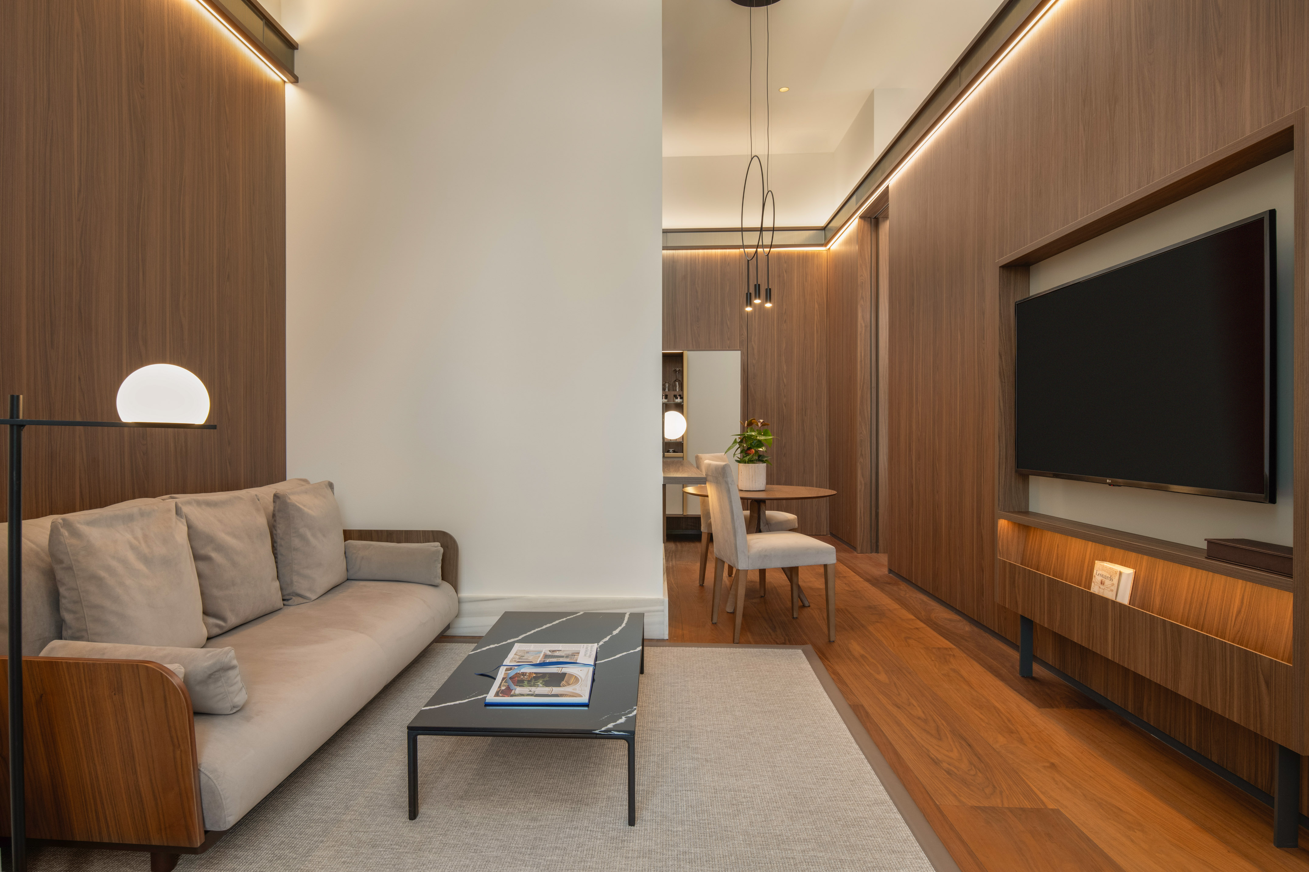 Contemporary living room with wood panels, beige sofa, coffee table, TV, and dining area.