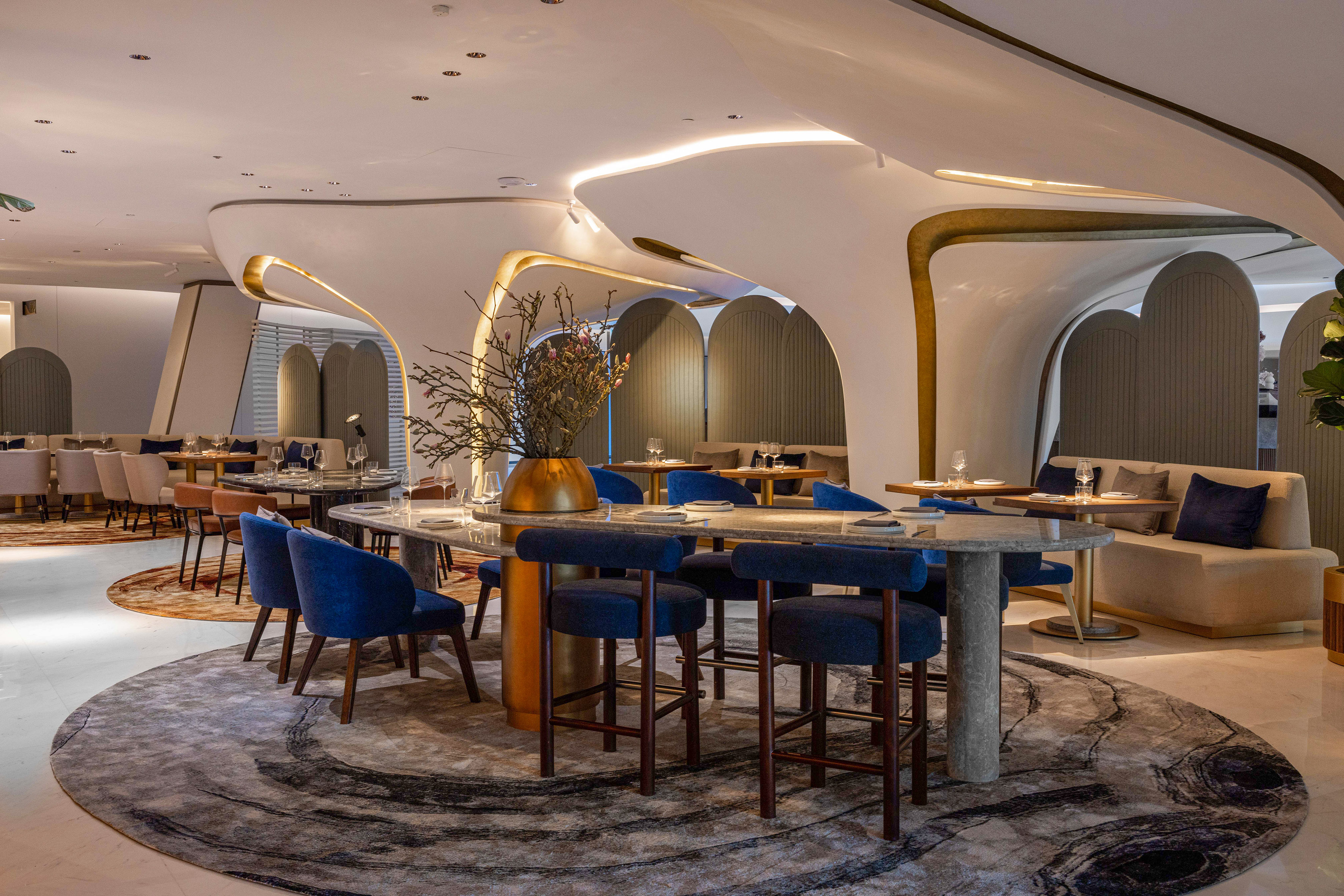 Elegant modern restaurant with curved architecture, blue chairs, and marble tables.