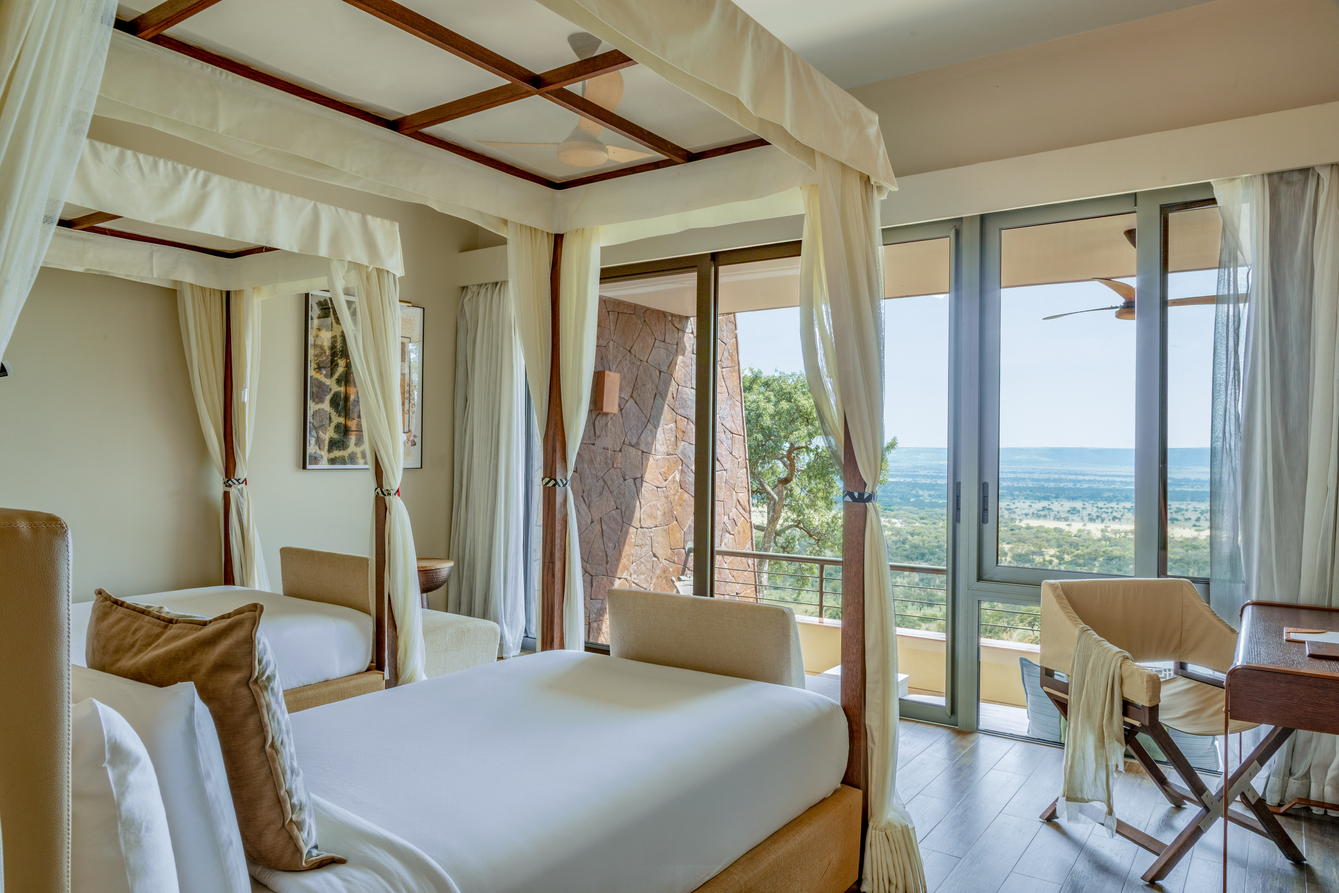 Luxury safari lodge room with two four-poster beds and a stunning savanna view.