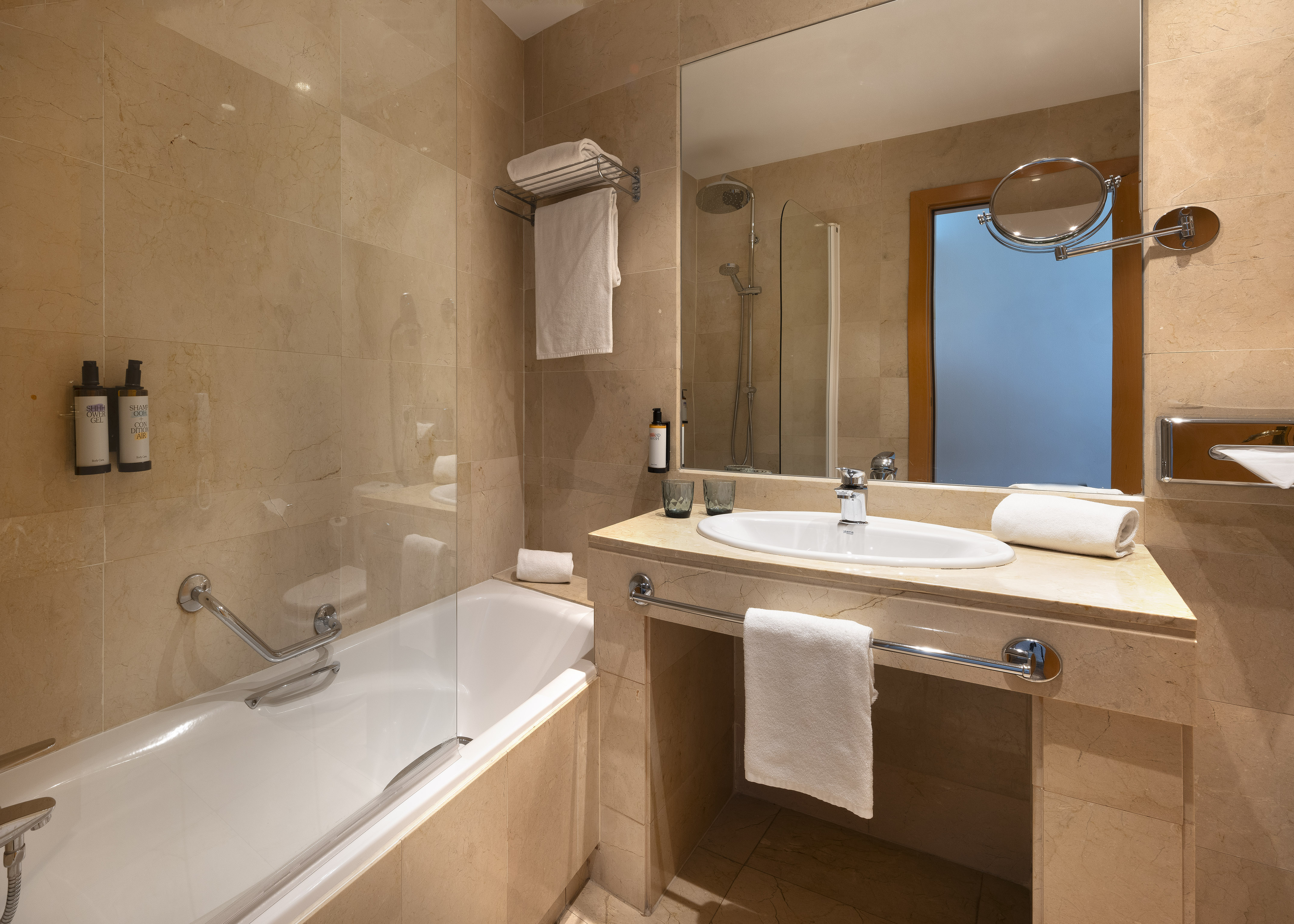 Modern tiled bathroom with bathtub, vanity sink, mirror, and white towels.