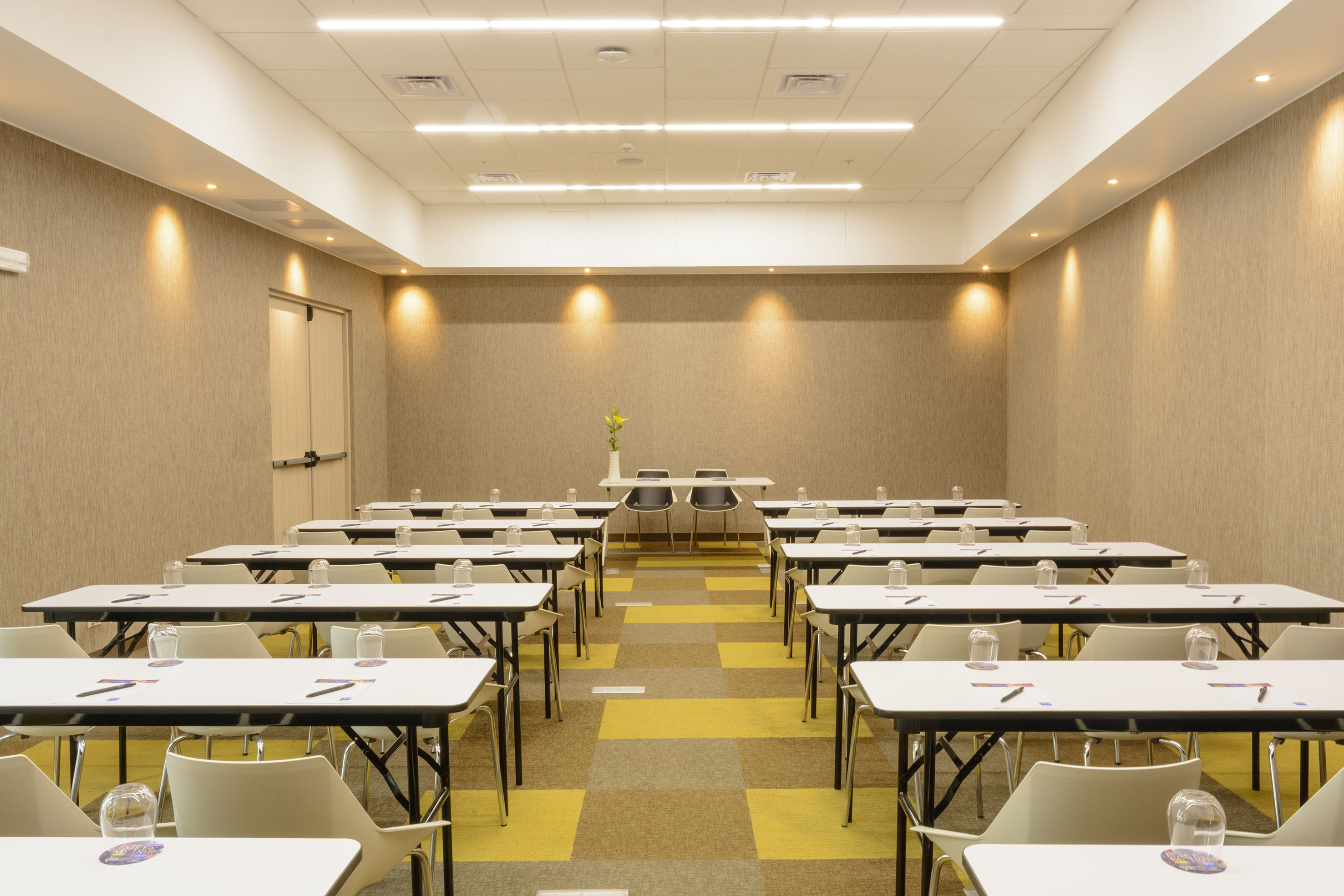Conference room with modern classroom setup, white tables, and yellow patterned carpet.