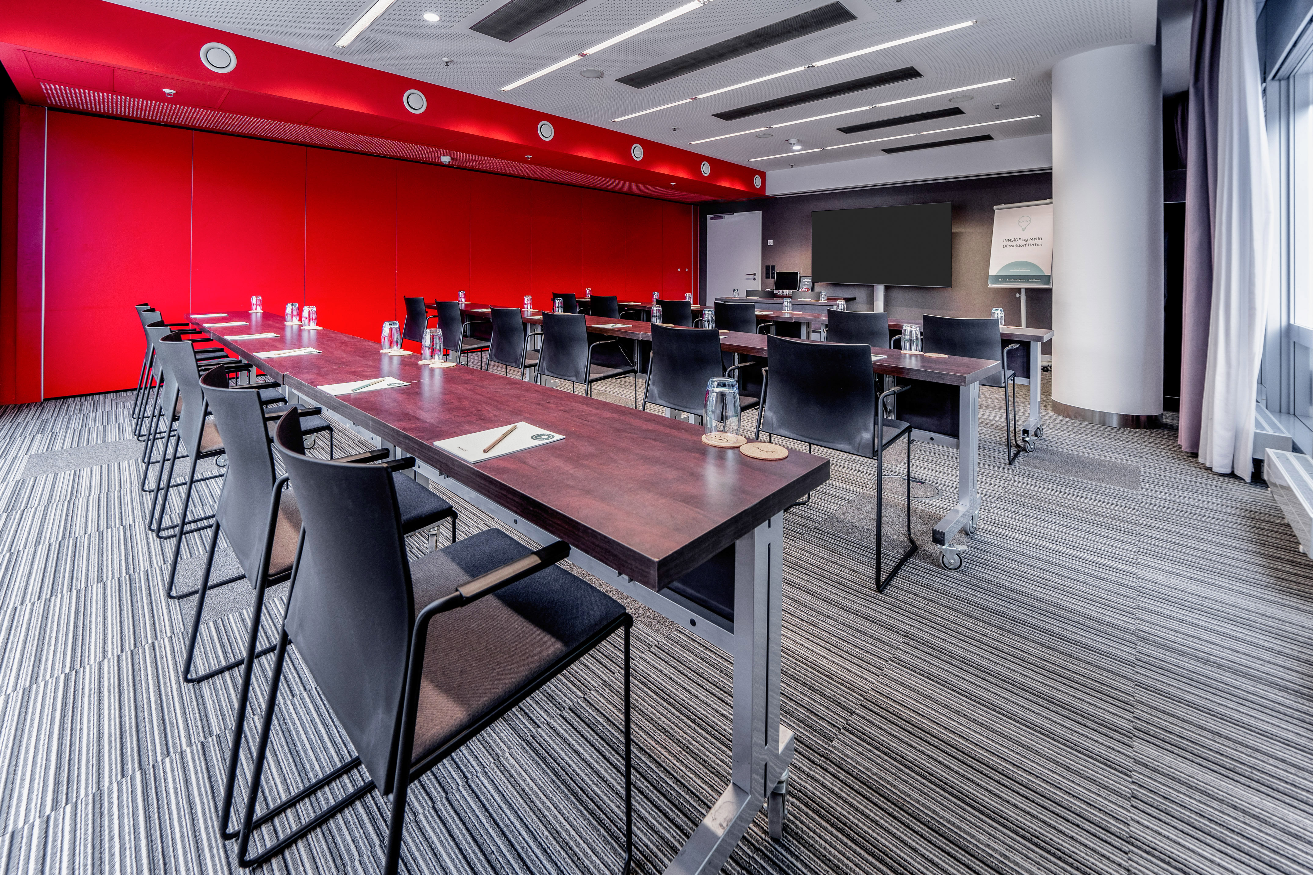 Modern conference room with red wall, dark tables, and presentation screen.