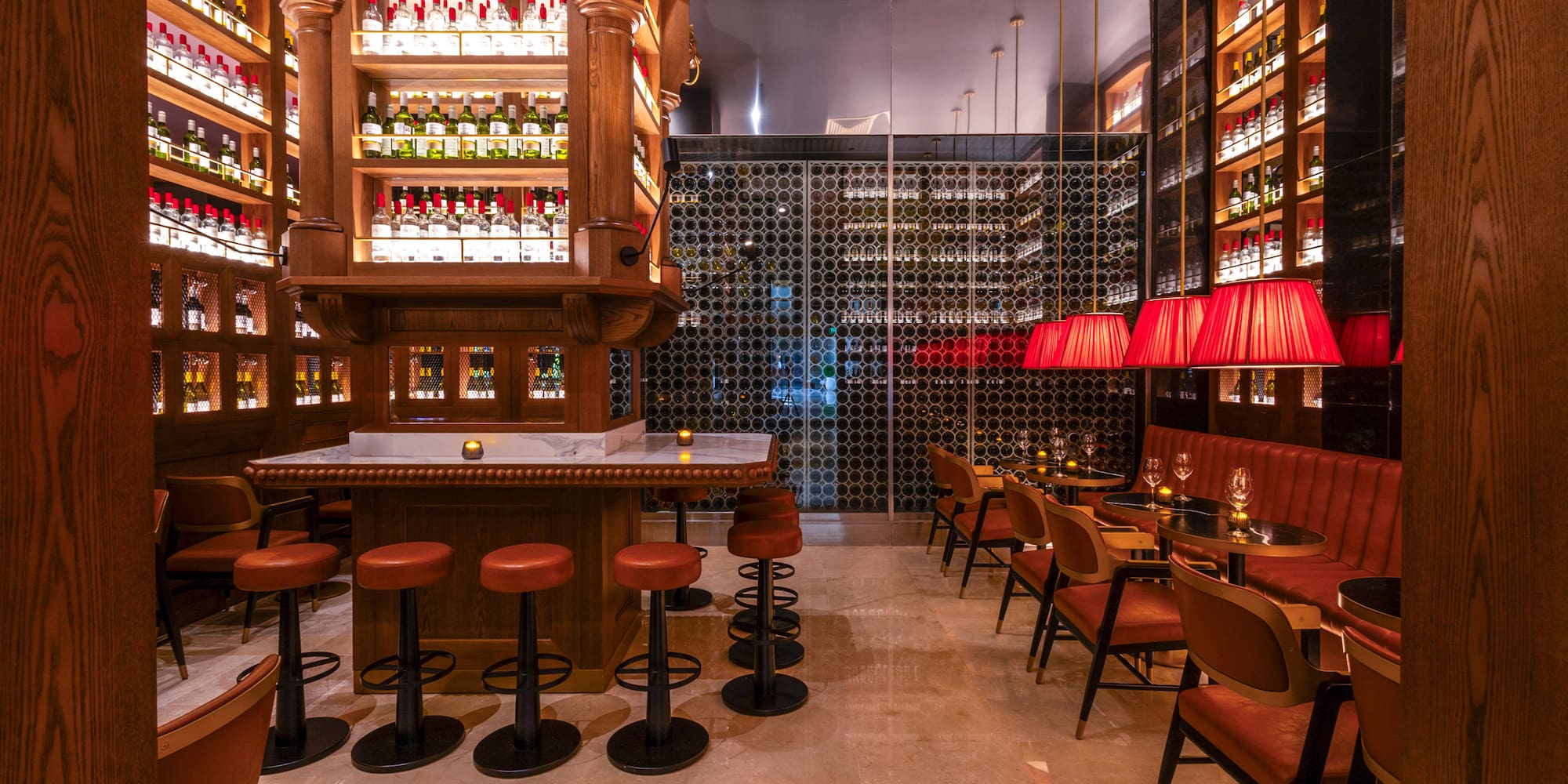 Elegant bar with wooden shelves of liquor, large wine cellar, and red lamps.