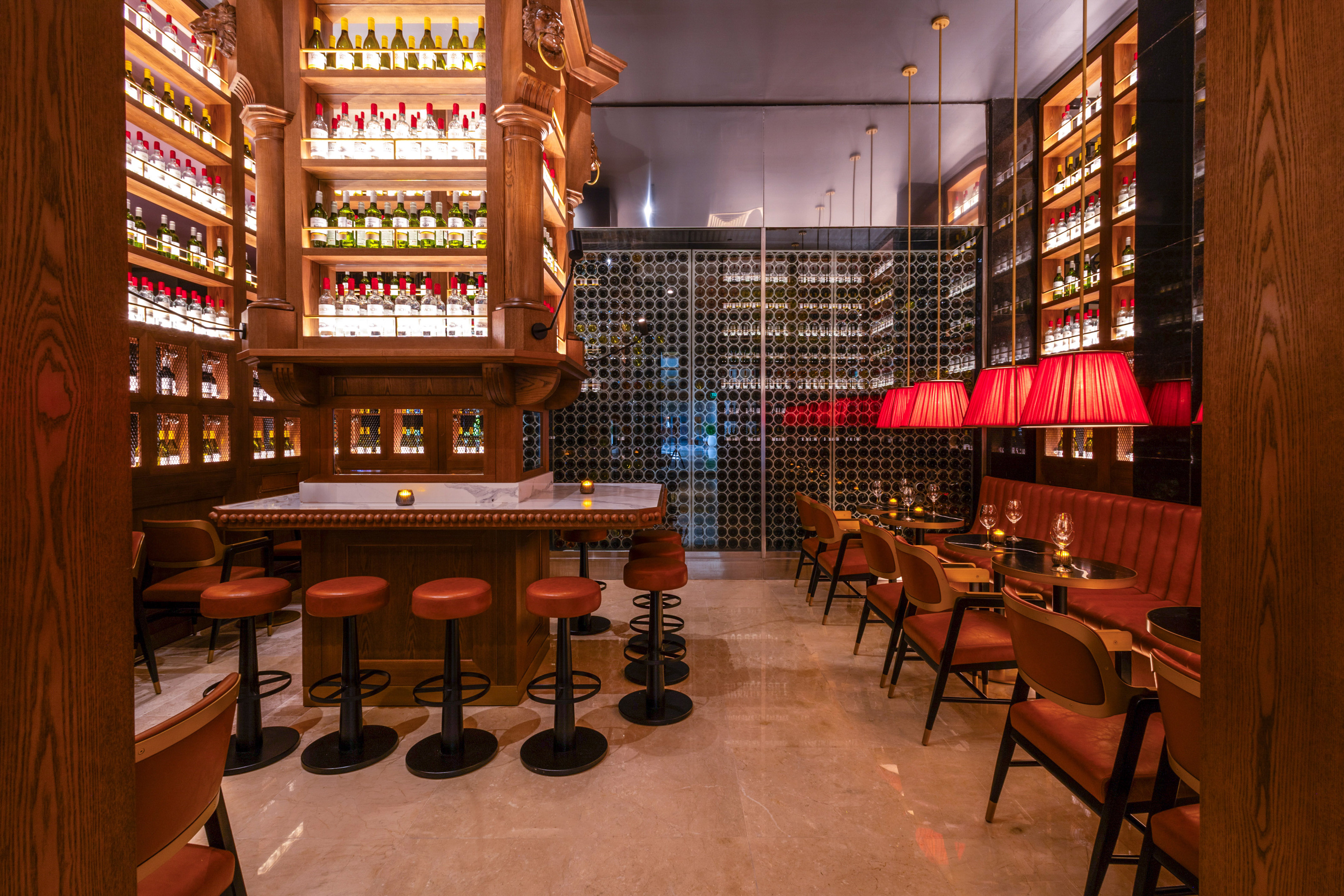 Elegant bar with wooden shelves of liquor, large wine cellar, and red lamps.
